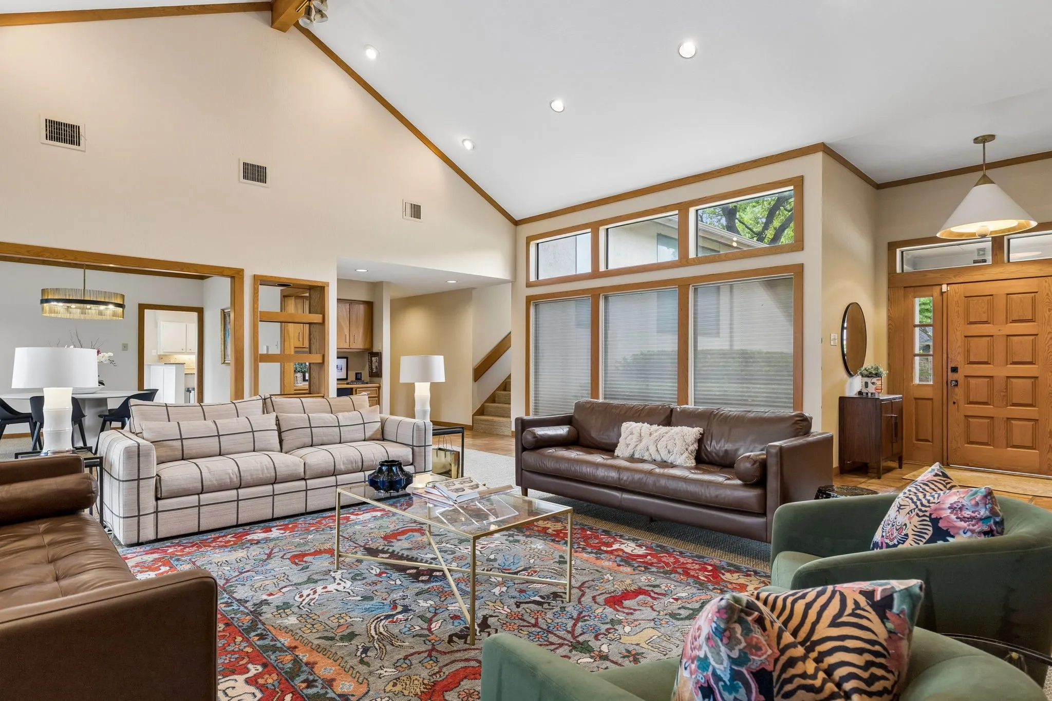 Spacious living area featuring a vaulted ceiling with exposed wood beams, recessed lighting, and a prominent wood-paneled entry door
