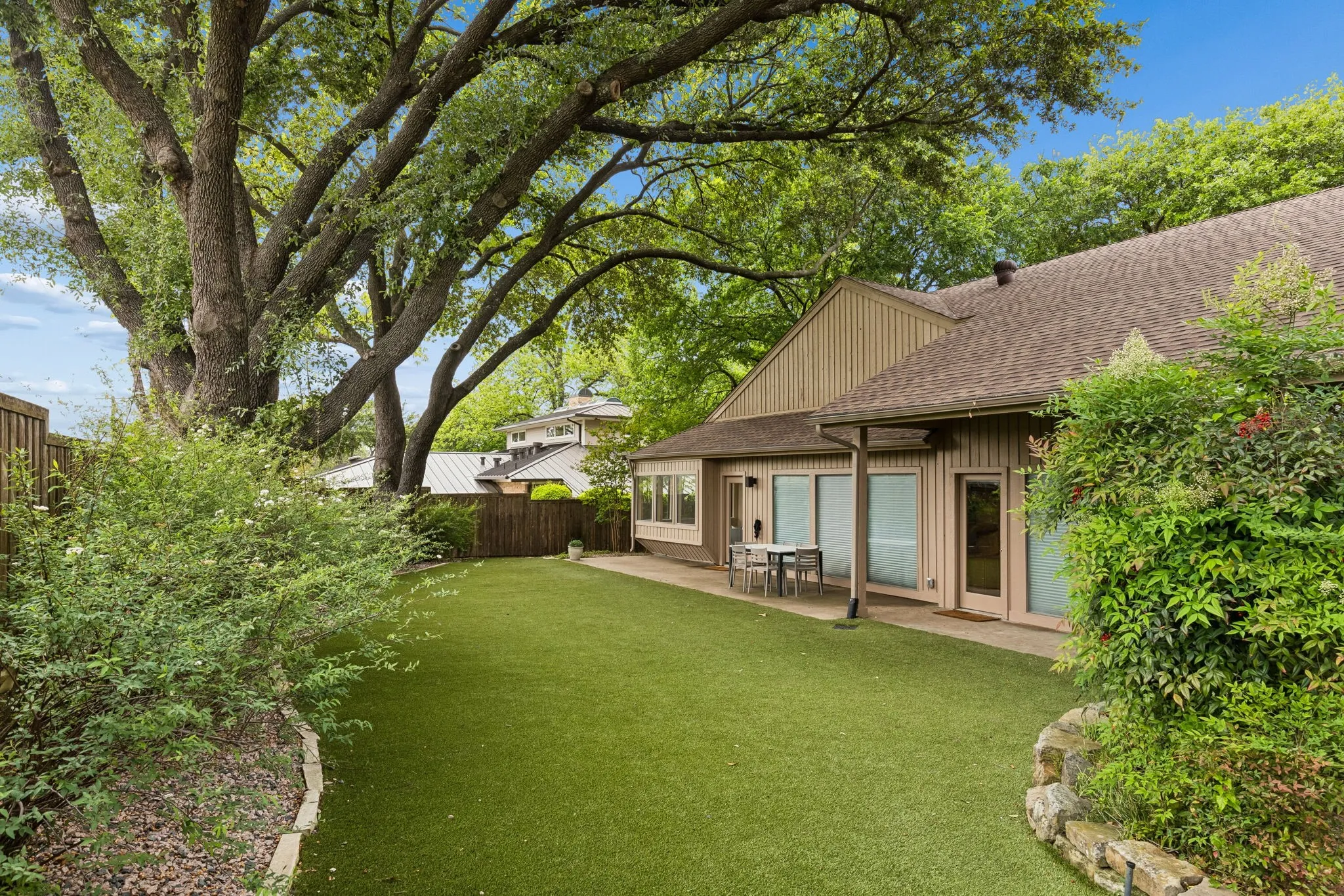 Expansive backyard featuring a manicured artificial lawn and a stone-edged garden bed