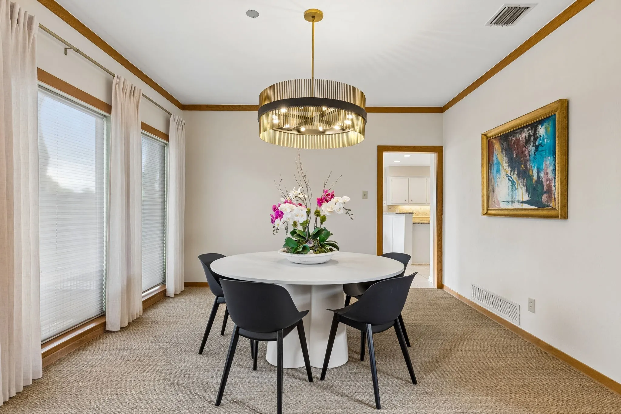 Dining space featuring a drum chandelier, three large windows with blinds, wood trim, and textured carpeting
