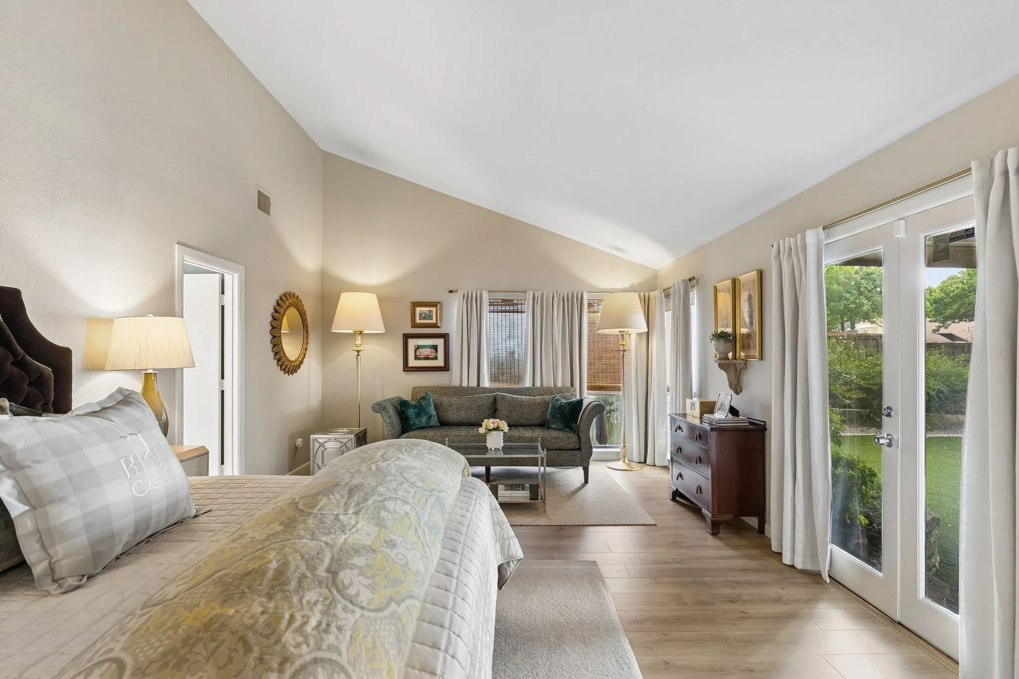 Vaulted ceilings enhance this spacious room featuring wood-finish flooring, multiple windows, and exterior French doors opening to the yard