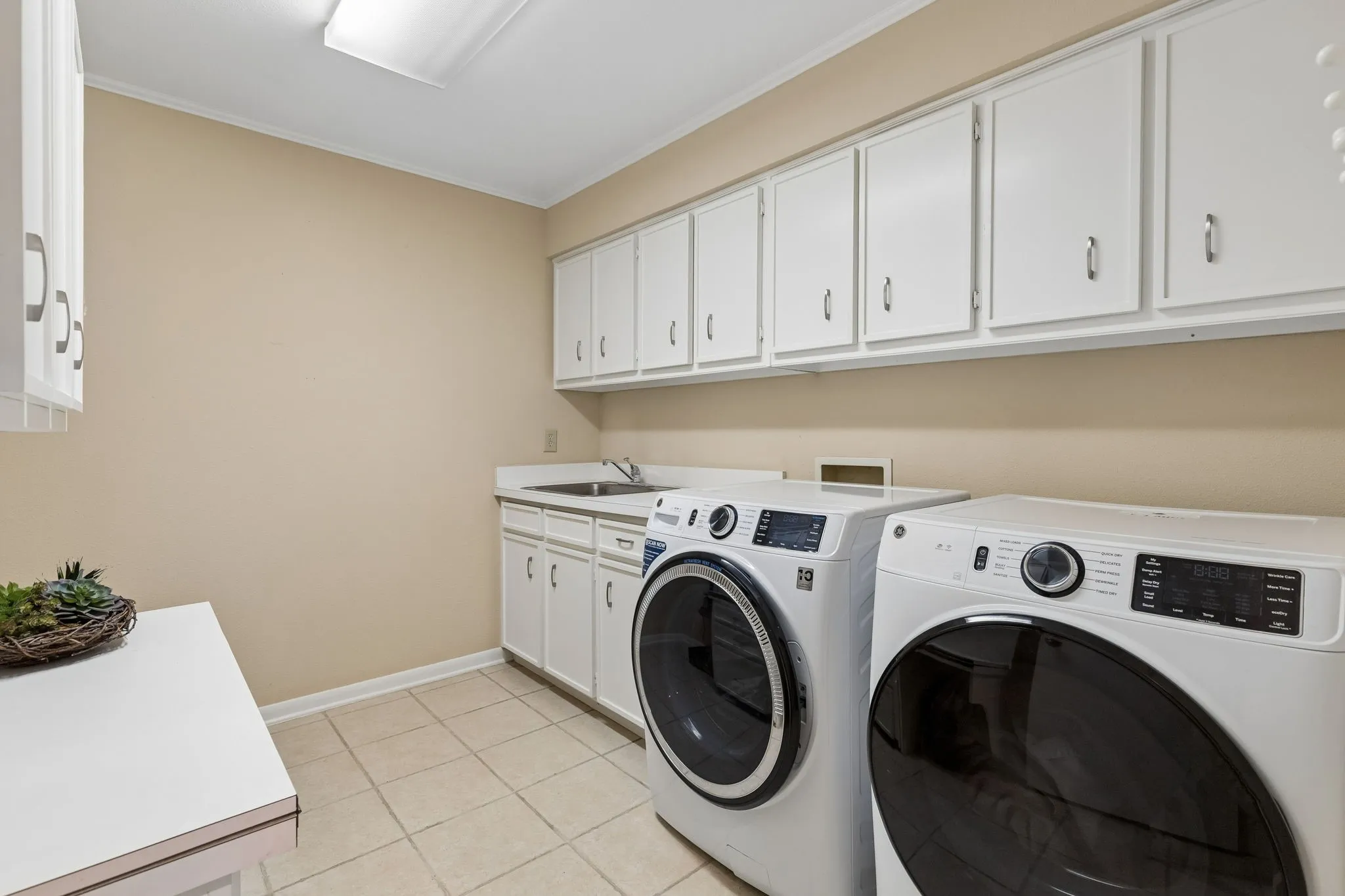 Spacious utility room featuring extensive white cabinetry, a built-in sink with countertop, and tile flooring
