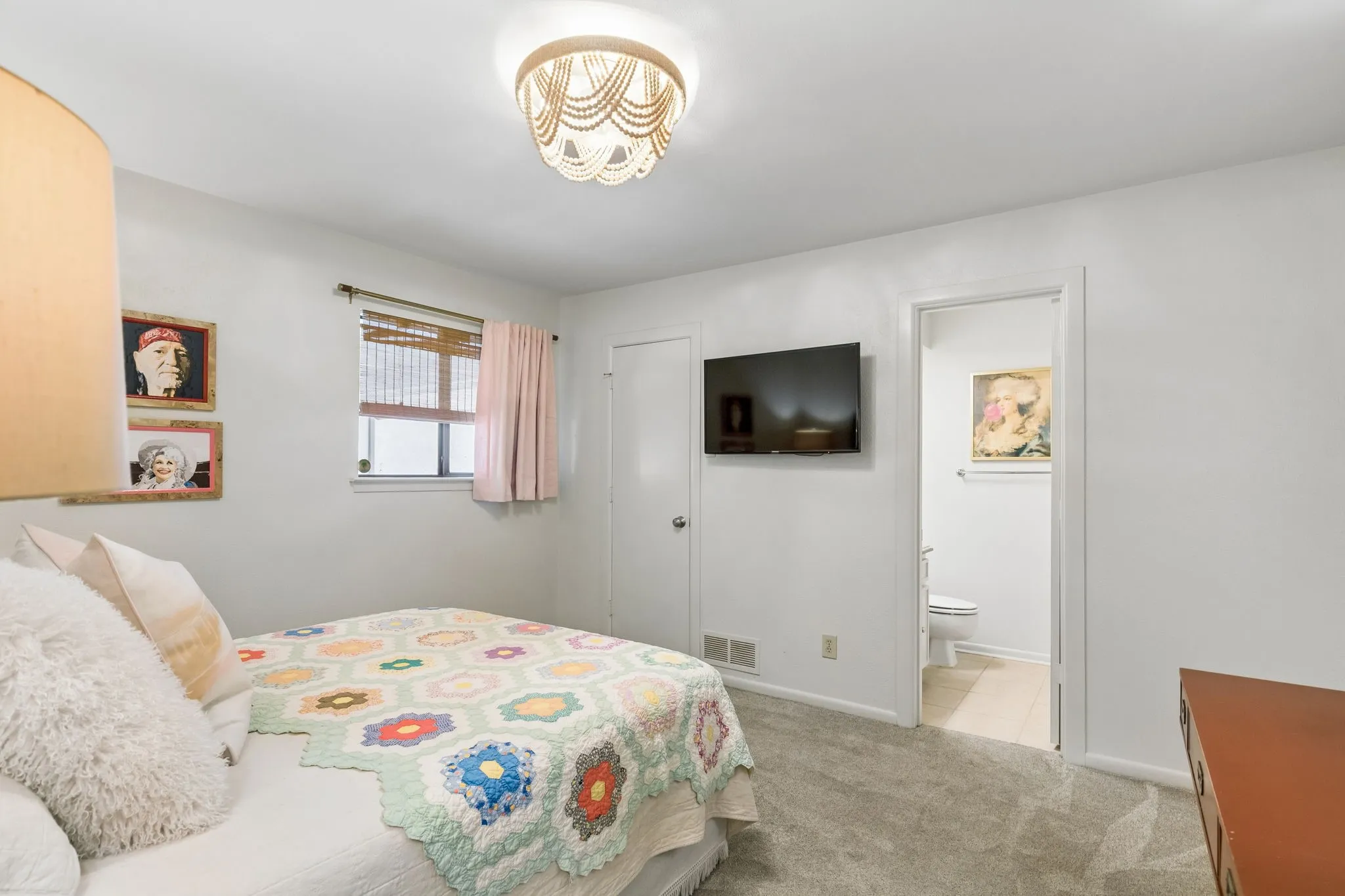 Carpeted bedroom featuring a ceiling-mounted light fixture, a window with blinds, and a door leading to an adjacent bathroom
