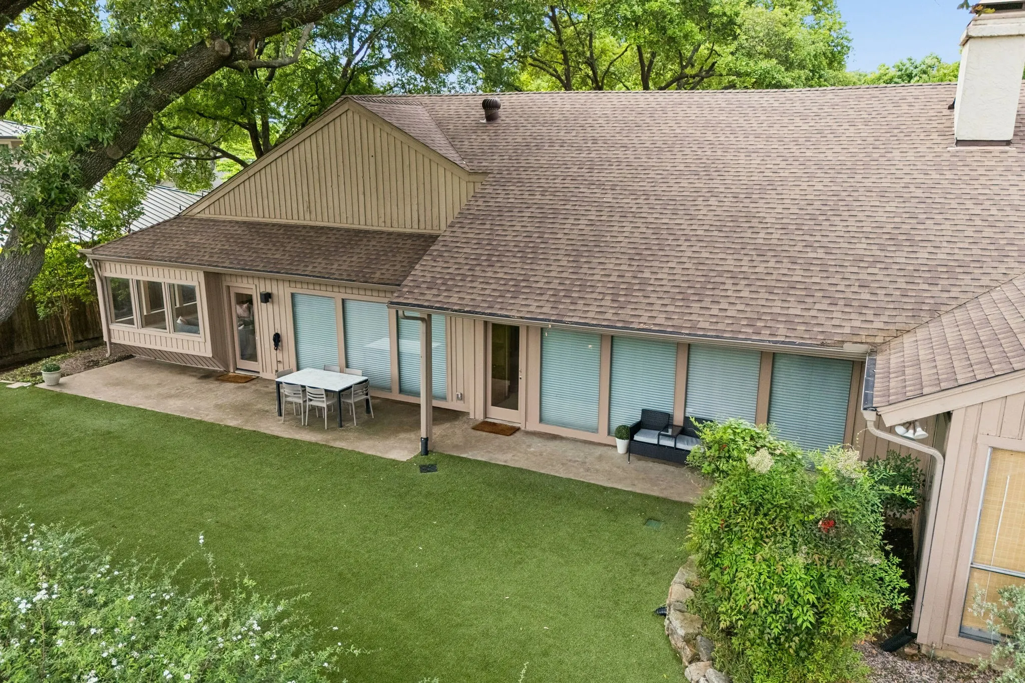 Expansive rear exterior featuring a concrete patio, artificial turf, and mature tree canopy