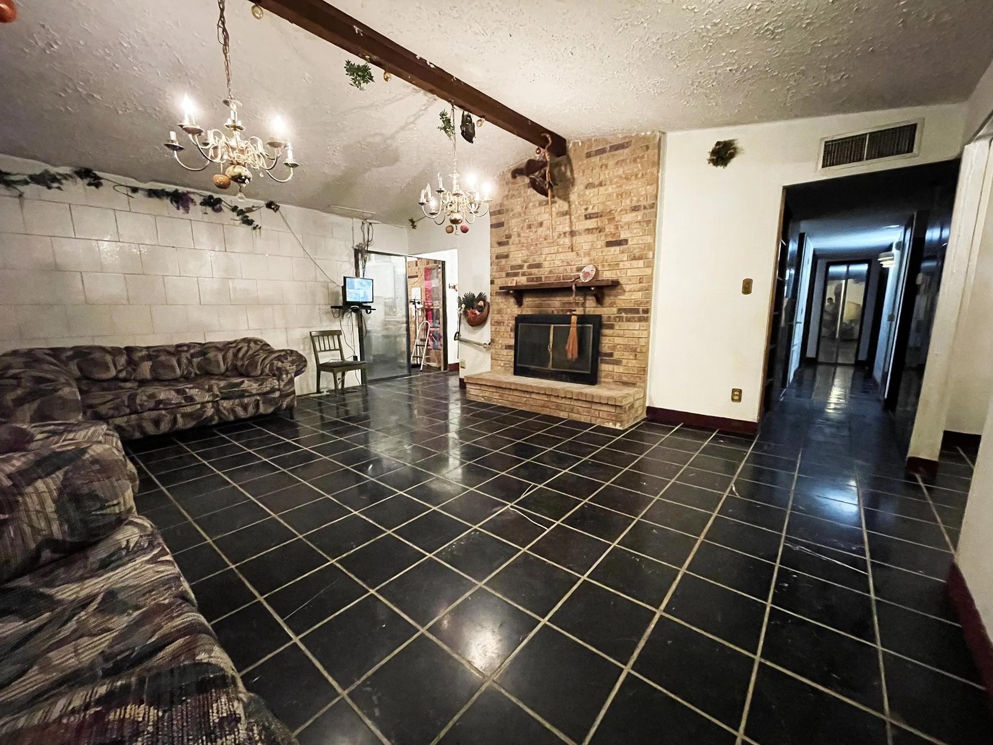 Spacious room featuring black tile flooring and a prominent brick fireplace with a wood mantle