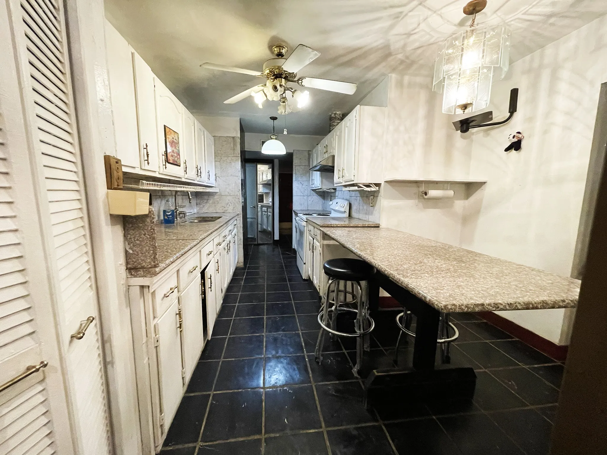 Galley kitchen featuring extensive white cabinetry, granite-finish countertops, and black tile flooring