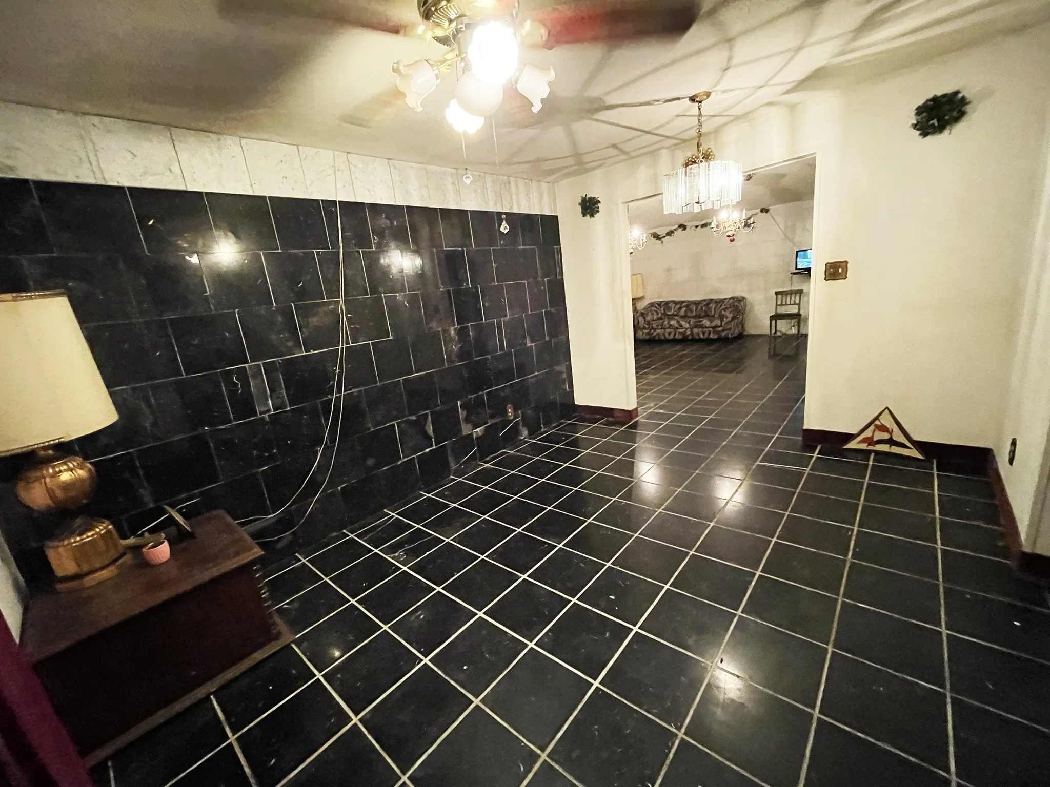Room featuring dark tile flooring, a dark tile accent wall, and a ceiling fan with light fixture