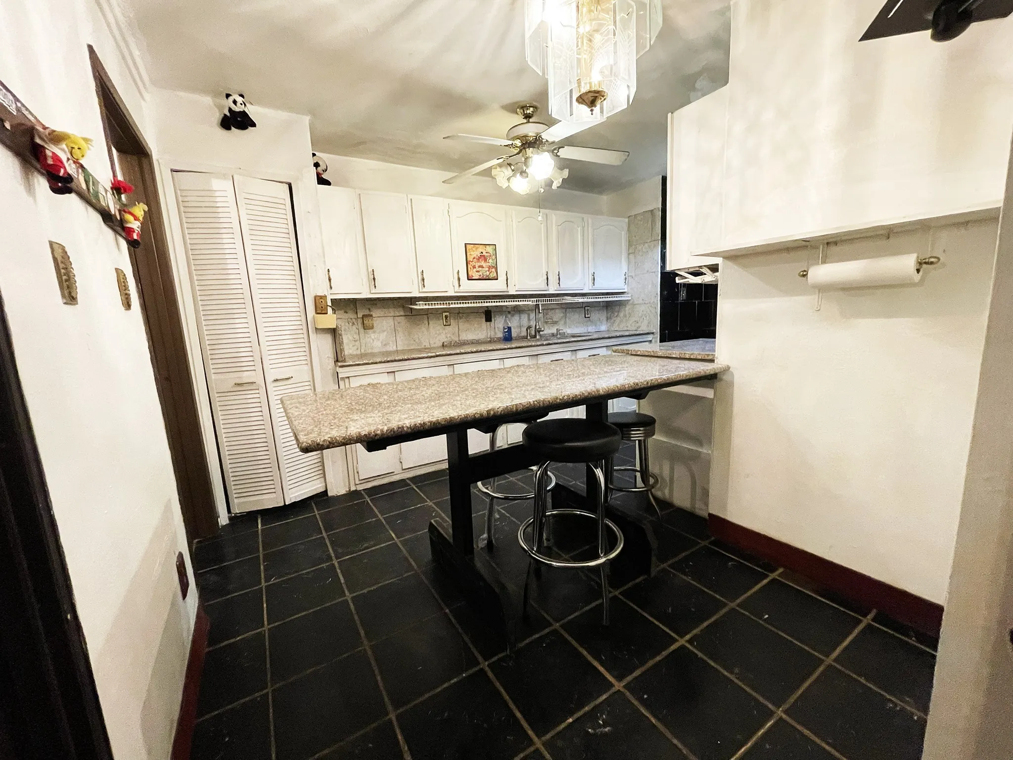 Kitchen featuring dark tile flooring, white cabinetry, a built-in breakfast bar with a stone-finish countertop, and ceiling-mounted lighting