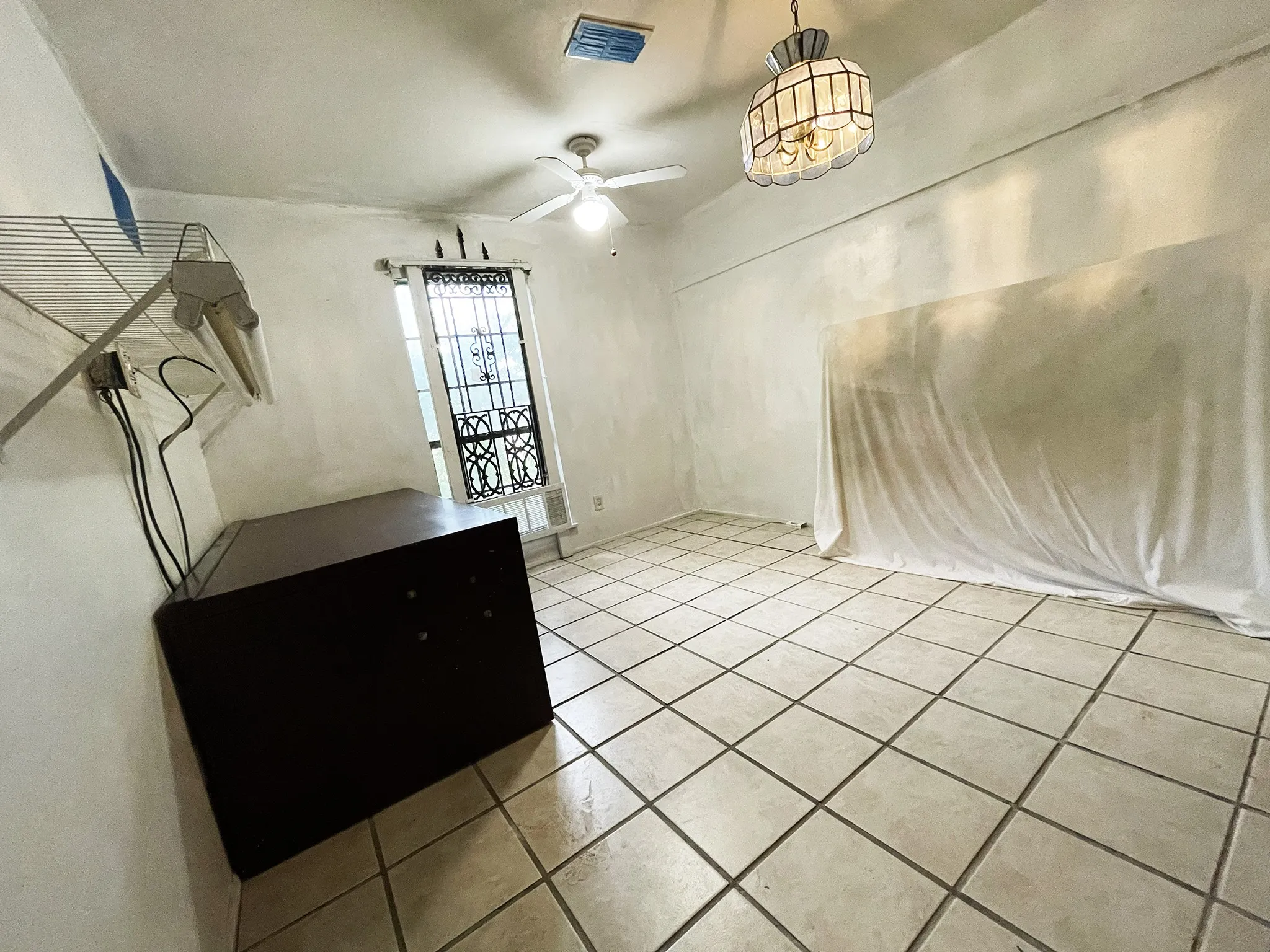 Spacious room featuring light-toned tile flooring, a ceiling fan, and an ornate window with security bars