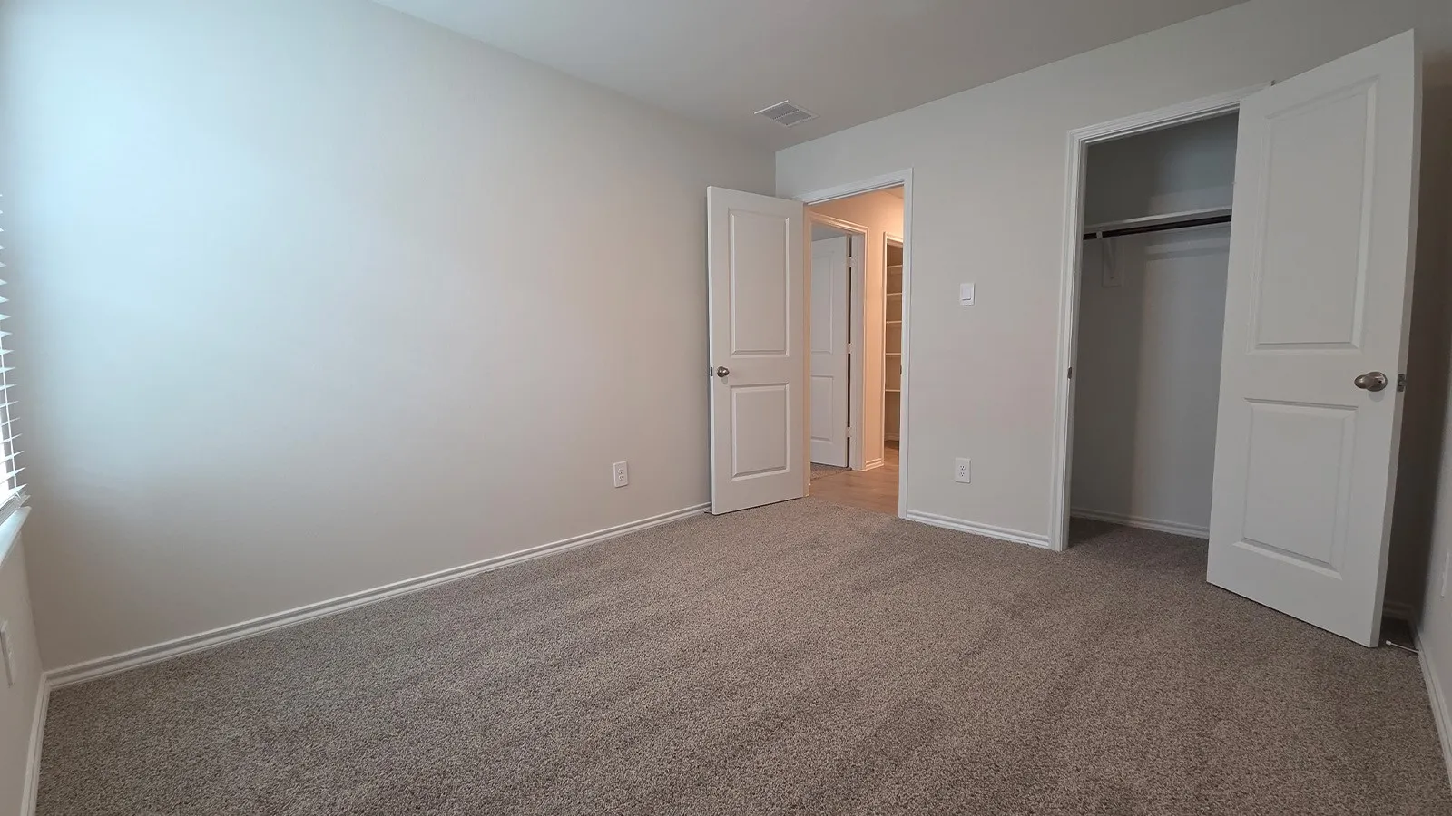 Carpeted interior room featuring neutral wall tones, baseboard molding, a window with blinds, and an open closet with a hanging rod