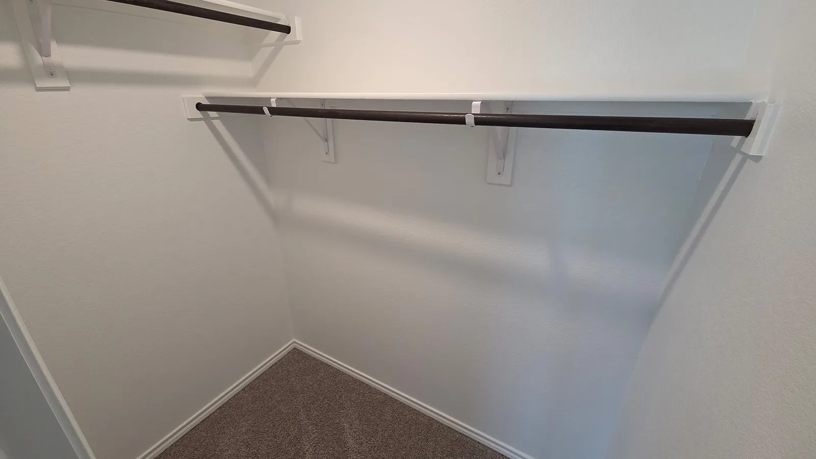 Walk-in closet with white walls, two integrated shelving units, and two dark-finish hanging rods