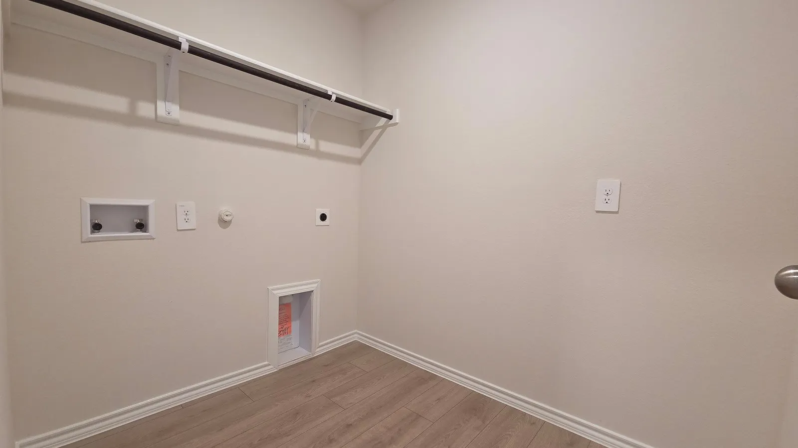 Dedicated utility space featuring light wood-finish flooring, white baseboards, and a wall-mounted clothing rod