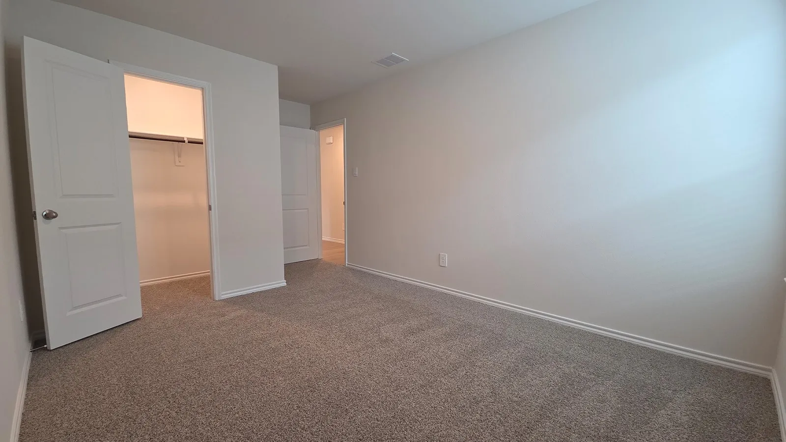 Neutral tone wall paint, textured carpet flooring, white baseboards, white trim doors, and a closet with a built-in rod