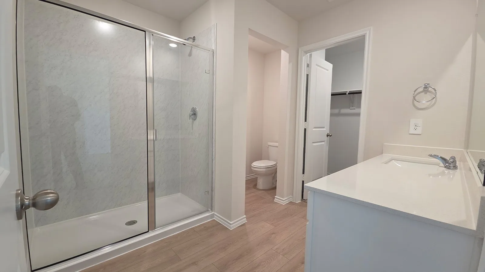 Bathroom featuring a glass-enclosed shower, single vanity with integrated sink, white countertop, and light wood-finish flooring