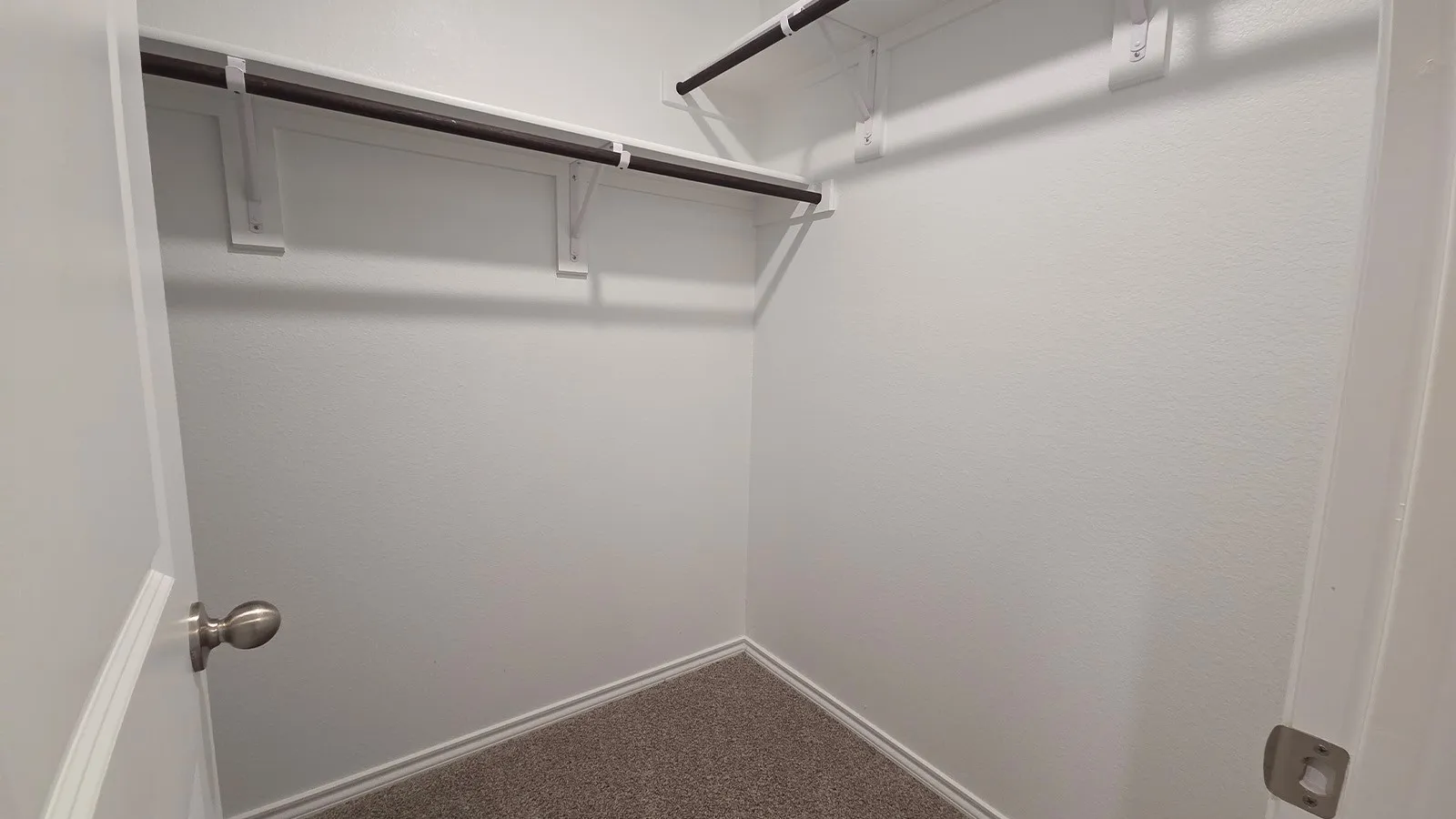 Walk-in closet featuring light gray carpeting, white walls, and dual-level hanging rods with shelving