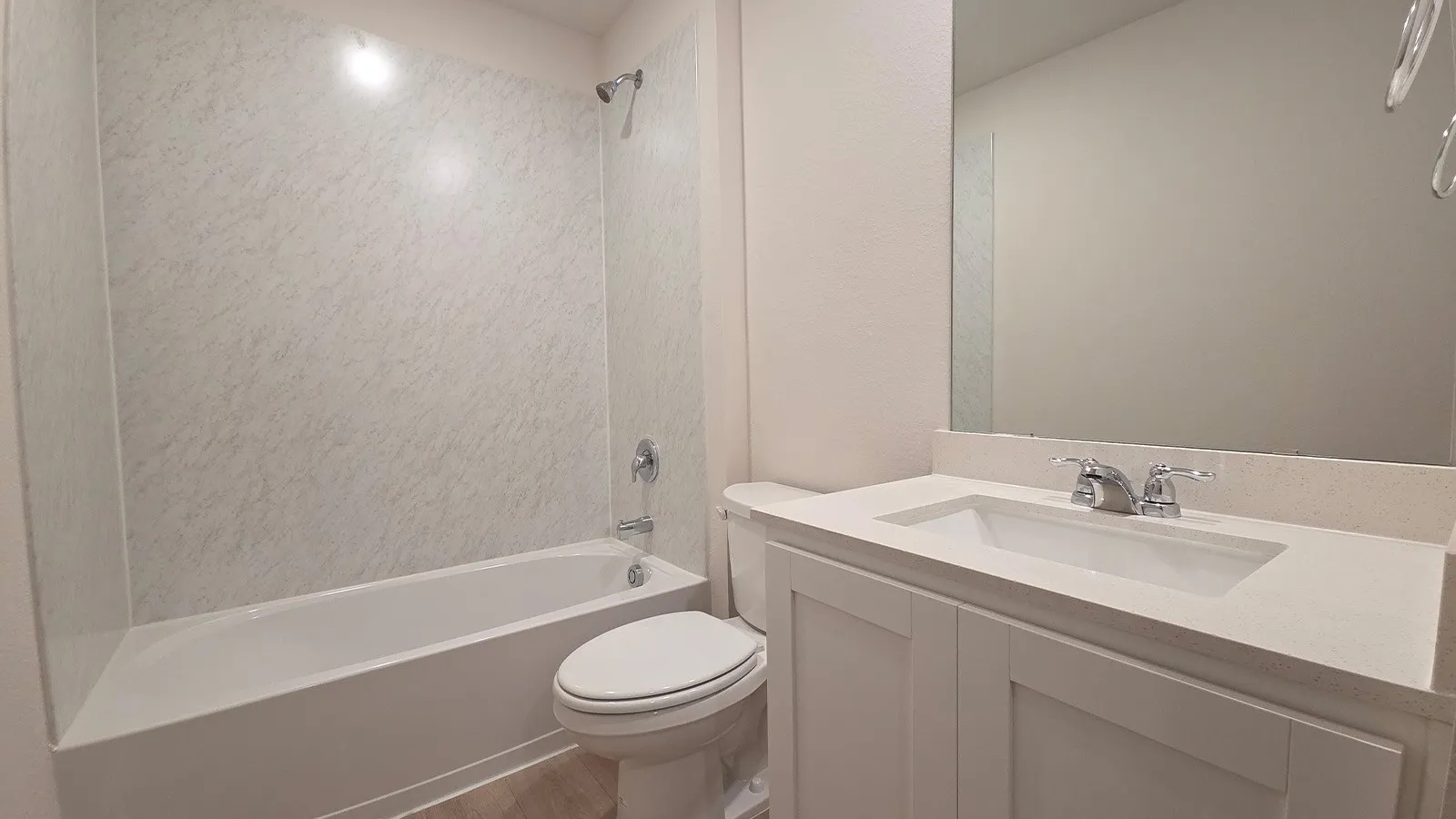 Bathroom featuring a white bathtub and shower surround, a white vanity with an integrated sink, a light-toned countertop, and chrome fixtures