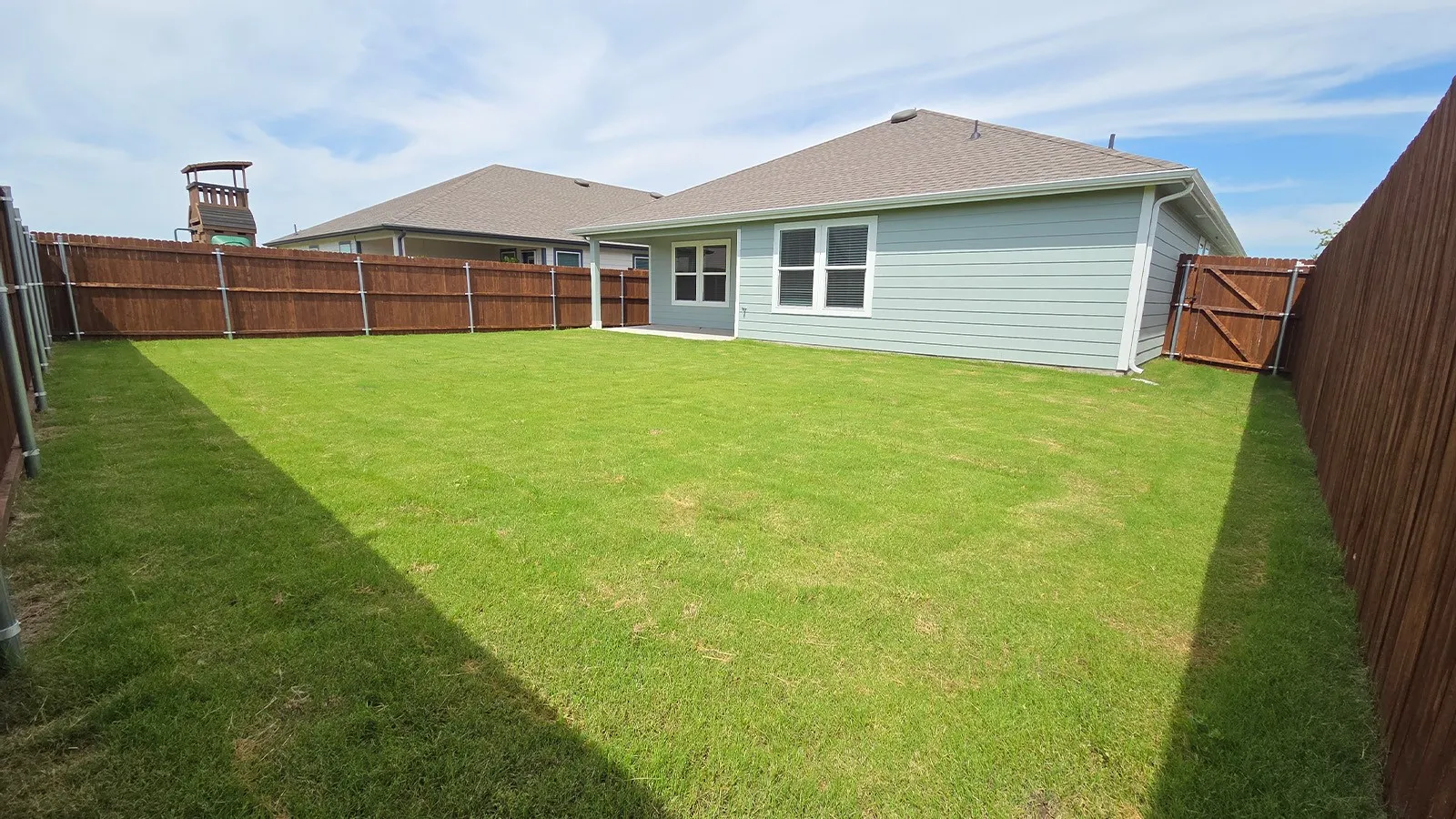 Expansive rear yard featuring a green lawn, privacy fencing, and a side access gate
