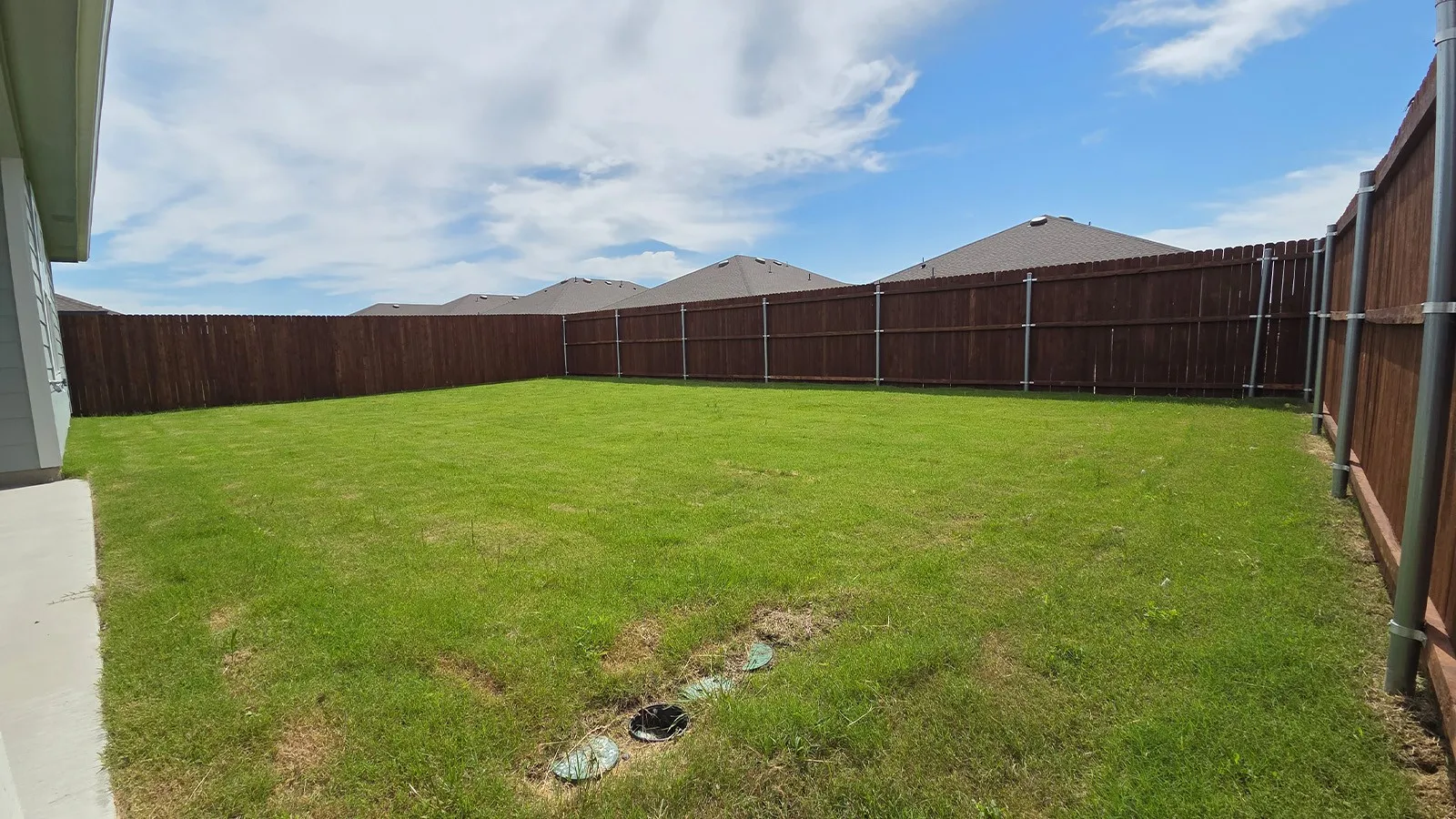Expansive backyard featuring a lush lawn, privacy fencing, and a concrete patio