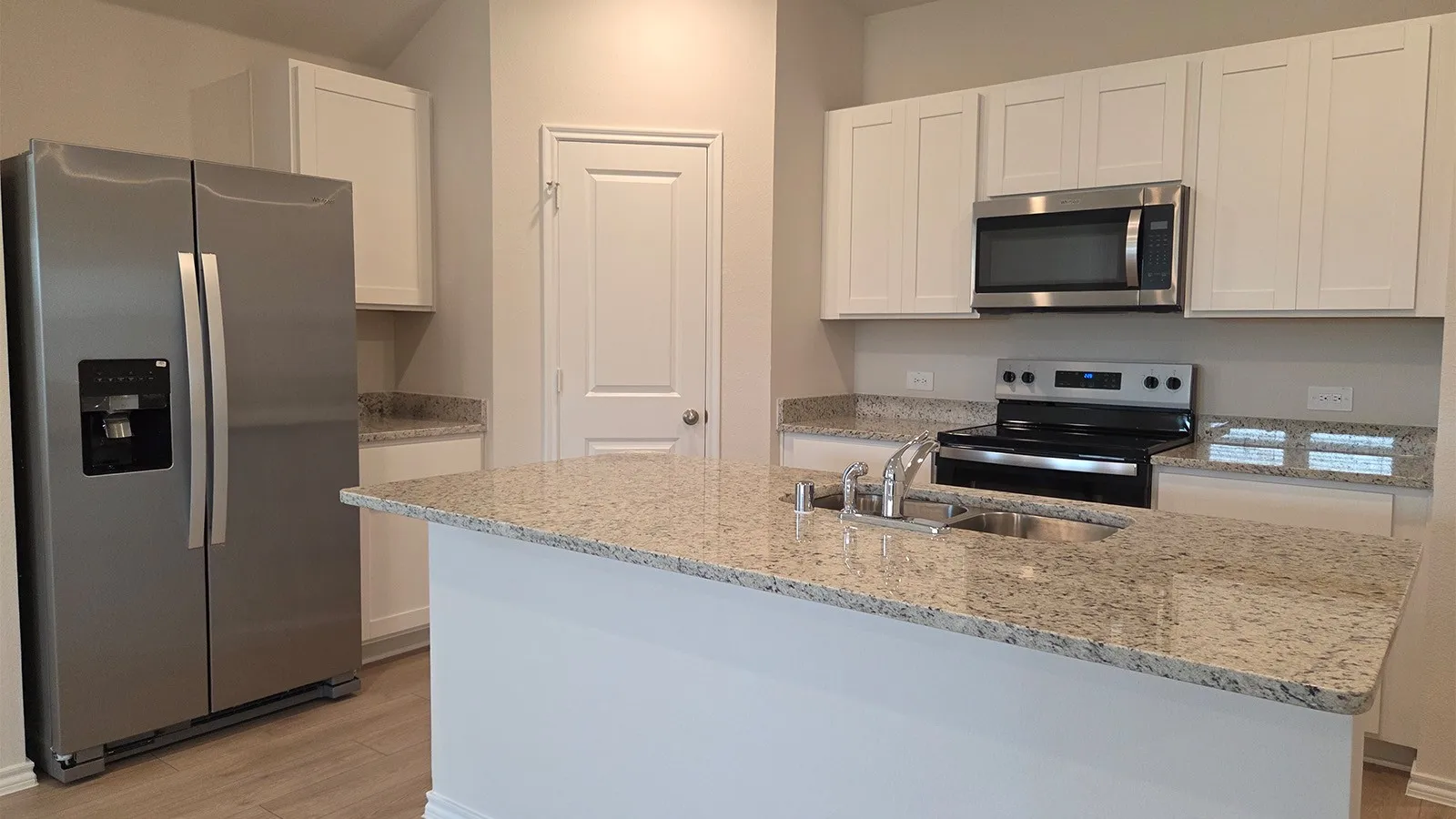 Kitchen featuring a central island with a double basin sink, granite countertops, white cabinetry, stainless steel appliances, and wood-finish flooring