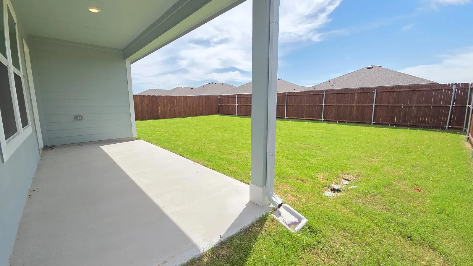 Covered patio with recessed lighting, concrete flooring, and a spacious grassy area enclosed by a privacy fence