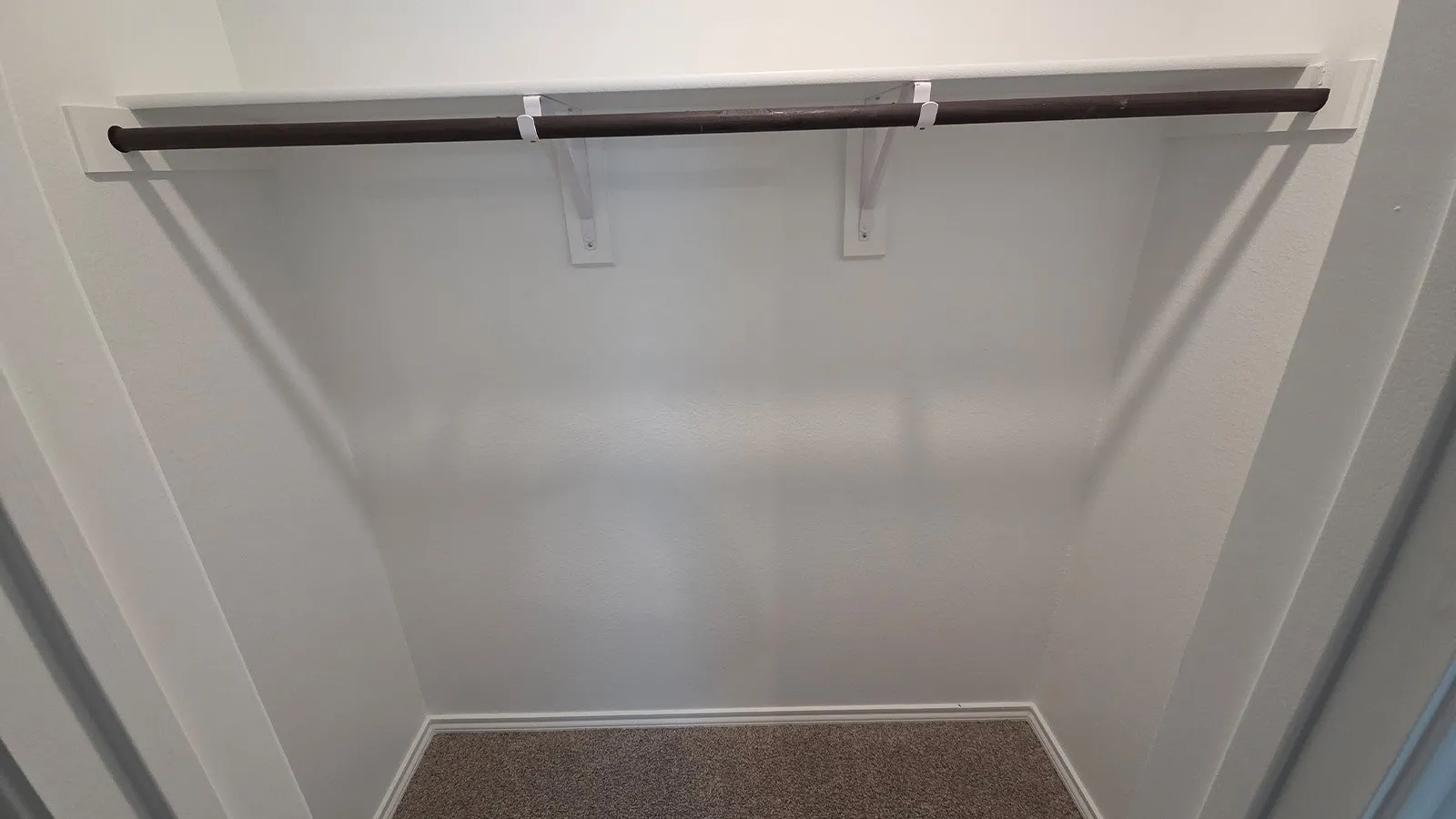 Recessed closet with a single hanging rod, upper shelf, white painted walls, and neutral carpet flooring