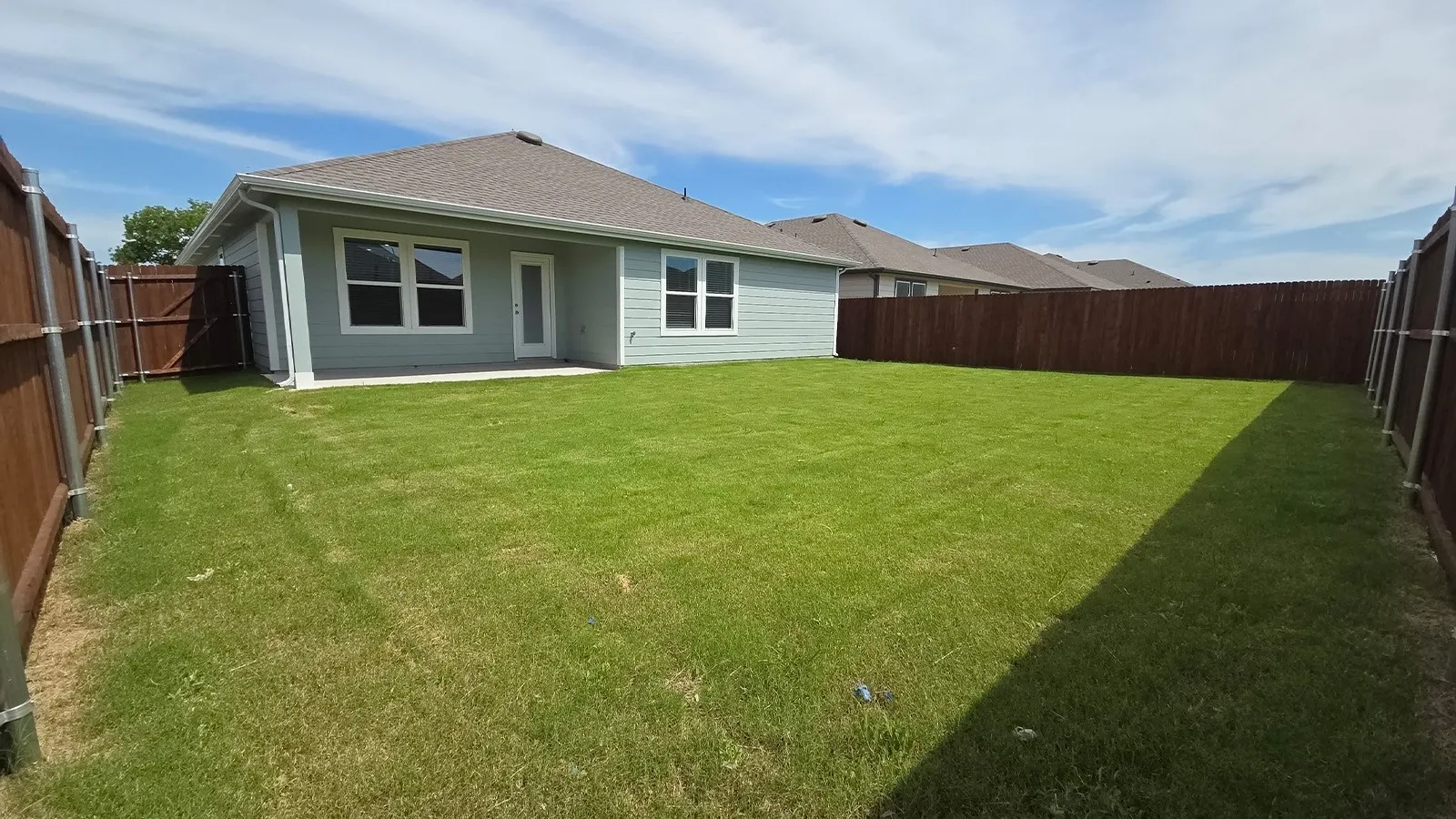 Expansive backyard featuring a manicured lawn, a concrete patio, and full perimeter fencing