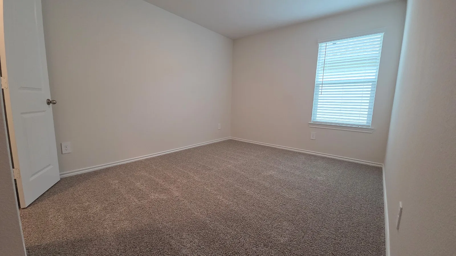 Carpeted room featuring a single window with blinds, white trim, and light-toned walls