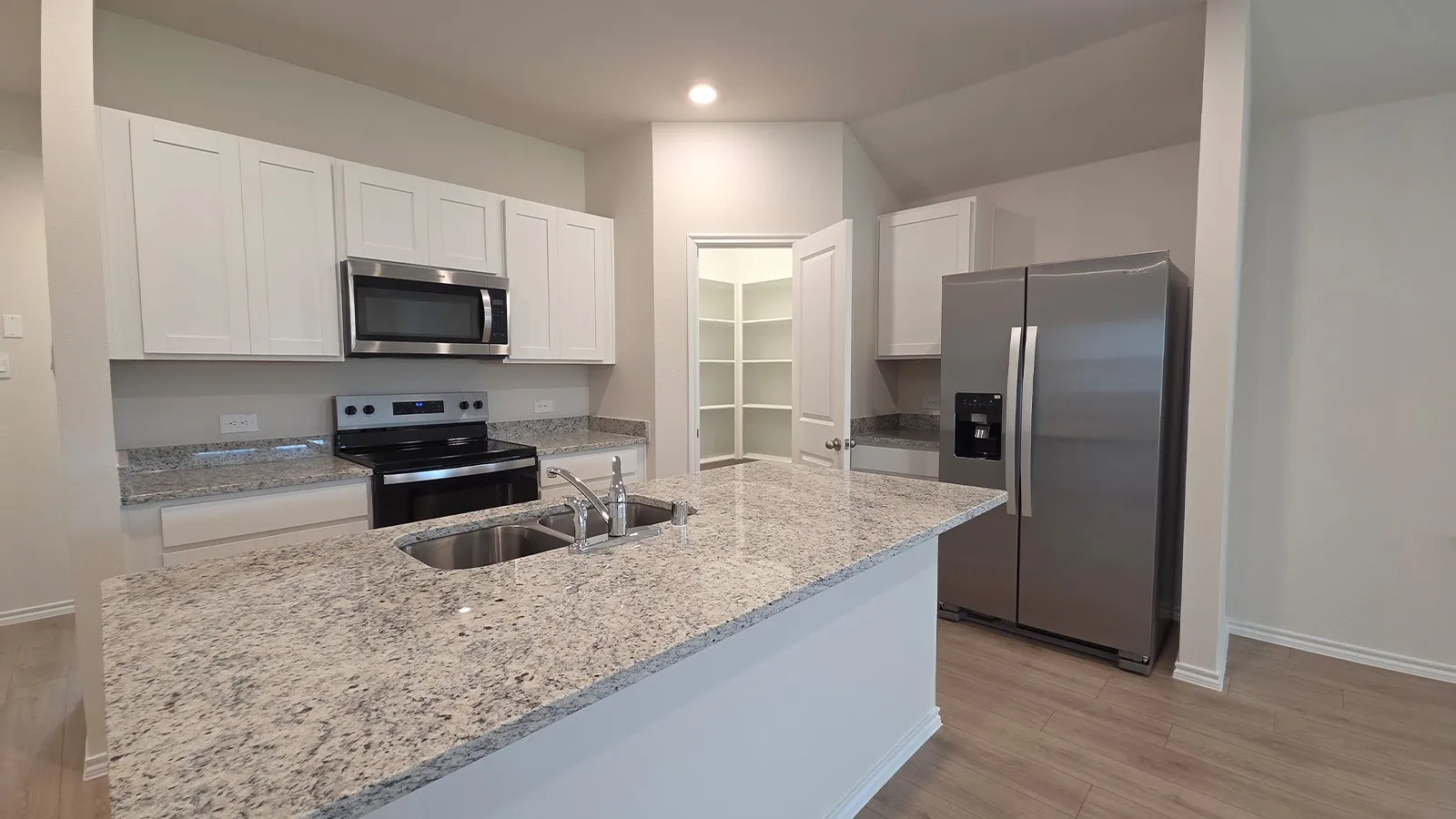 Kitchen featuring an expansive island with an undermount double basin sink, light-toned granite countertops, white shaker cabinetry, stainless steel appliances, and wood-finish flooring