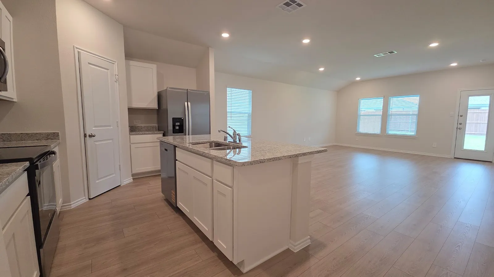 Open-concept kitchen and living area featuring wood-finish flooring, recessed lighting, white cabinetry, granite countertops, and stainless steel appliances