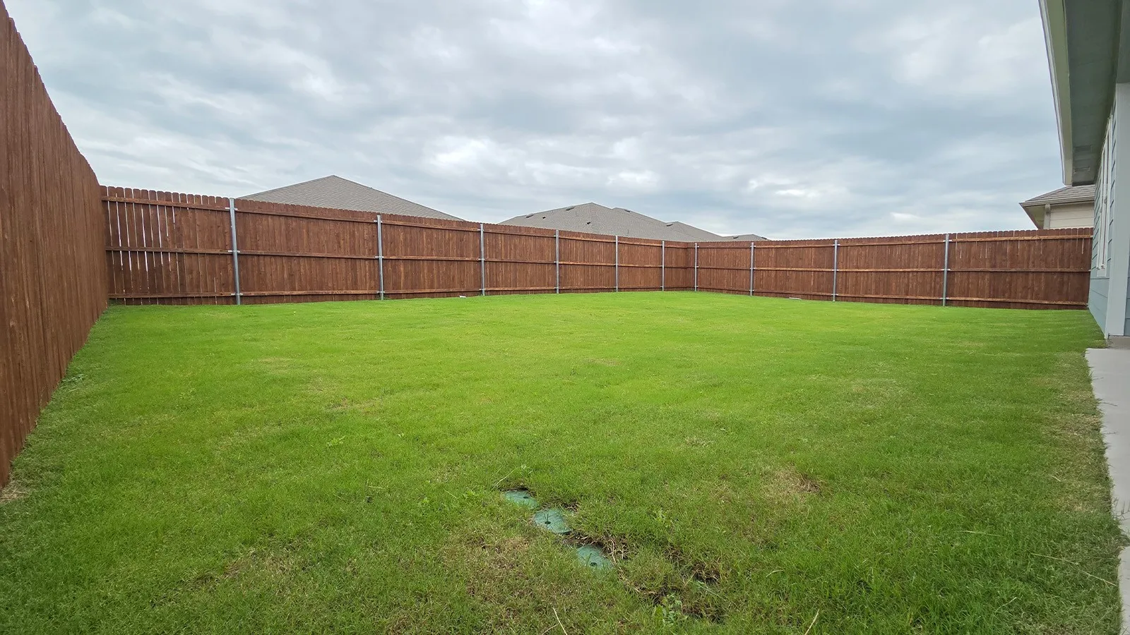 Expansive backyard featuring a lush green lawn, full wood privacy fencing, and a concrete patio area
