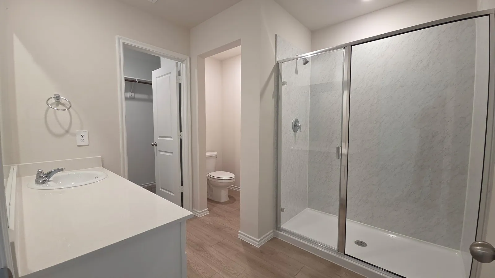 Full bathroom featuring a single vanity with an undermount sink and light-toned countertop, a separate water closet, a glass-enclosed shower with a white base, and wood-finish flooring