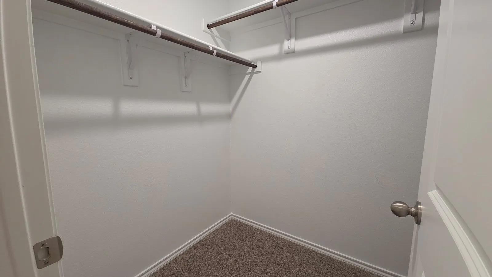 Closet featuring white textured walls, two levels of shelving, two clothes hanging rods, and neutral-toned carpet