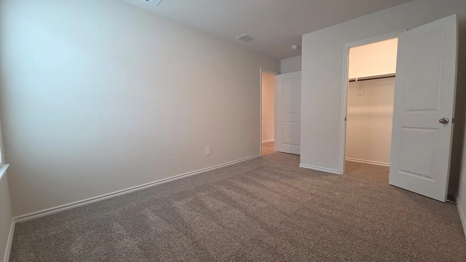Carpeted room featuring neutral wall tones, white trim, a double-door closet with shelving and hanging rod, and additional doorway access