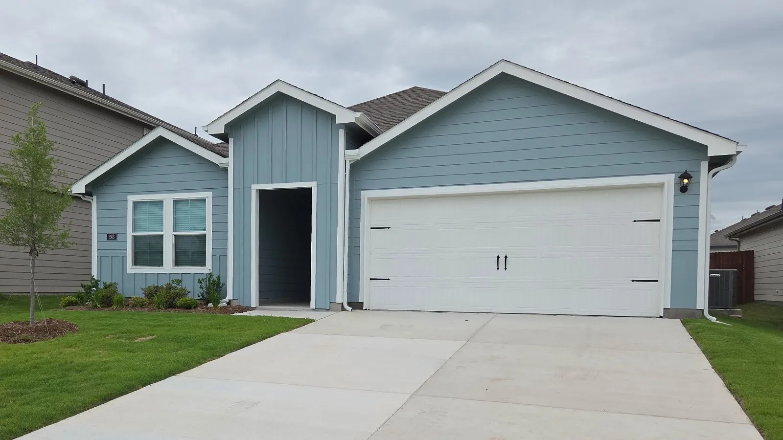 Light blue exterior with white trim, featuring a two-car garage with decorative hardware, a covered entry, and a manicured front lawn