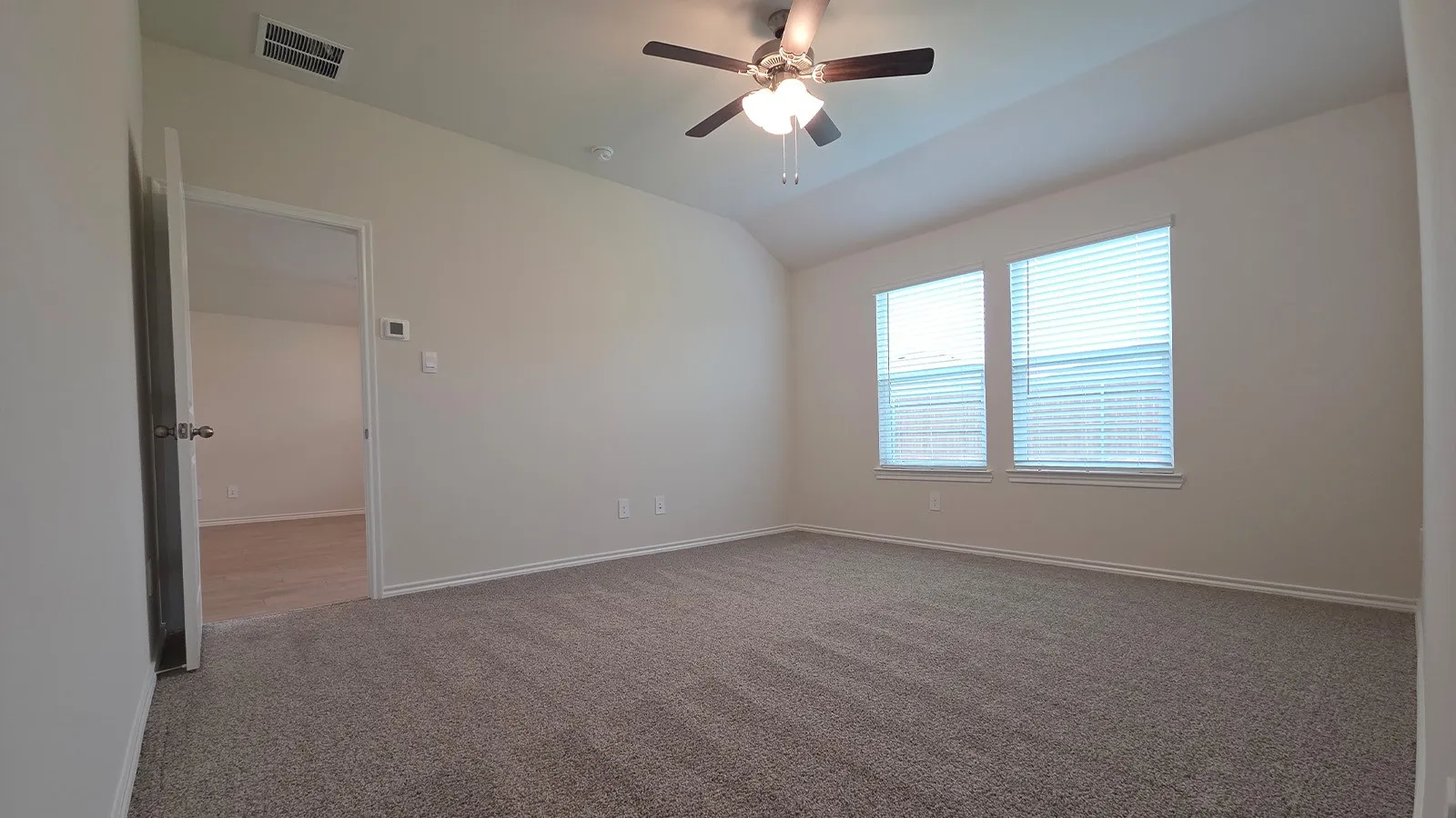 Carpeted room featuring a vaulted ceiling with a ceiling fan, two windows with blinds, and white baseboards