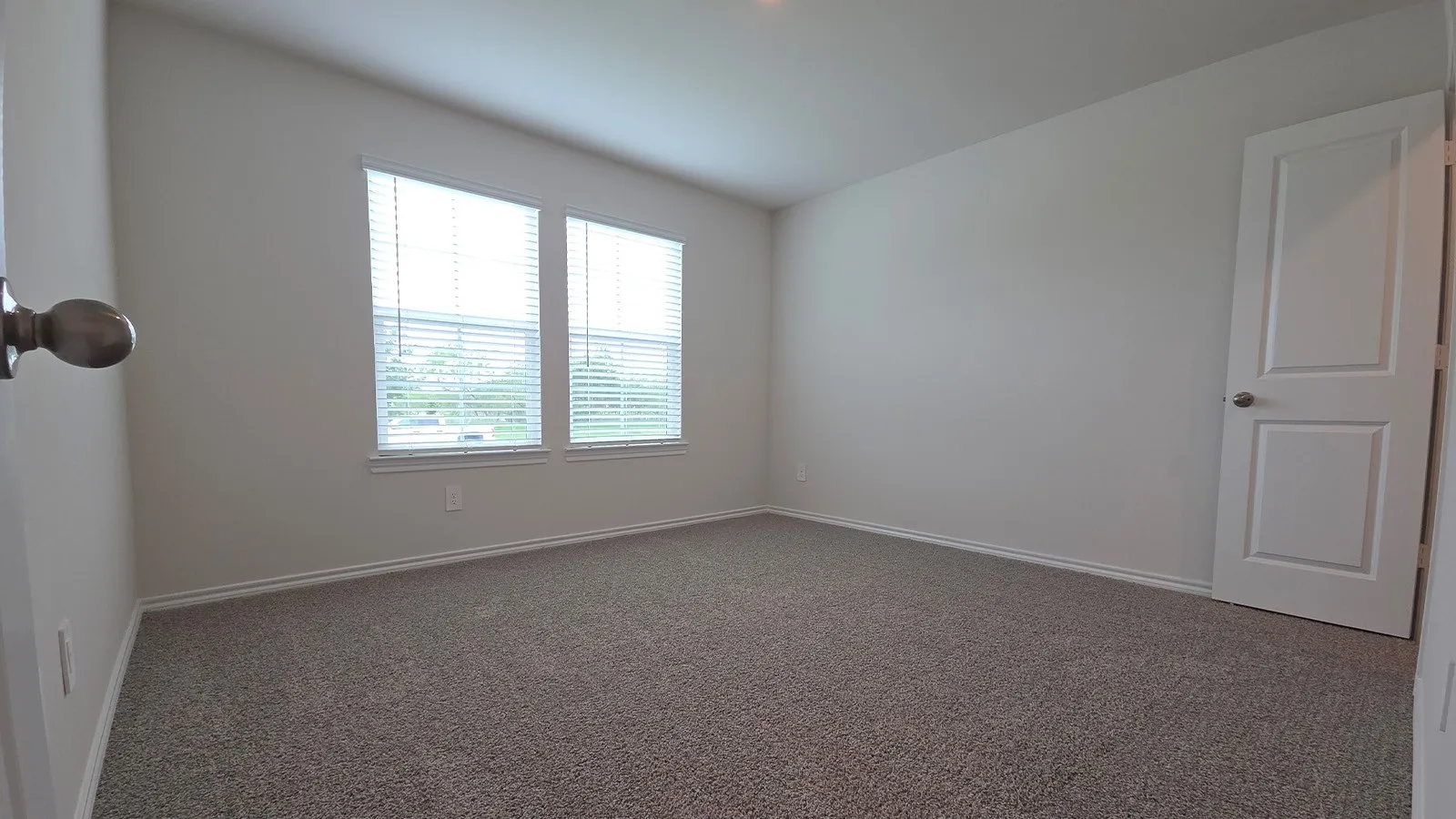 Carpeted room featuring two windows with blinds, a paneled door, and neutral wall paint