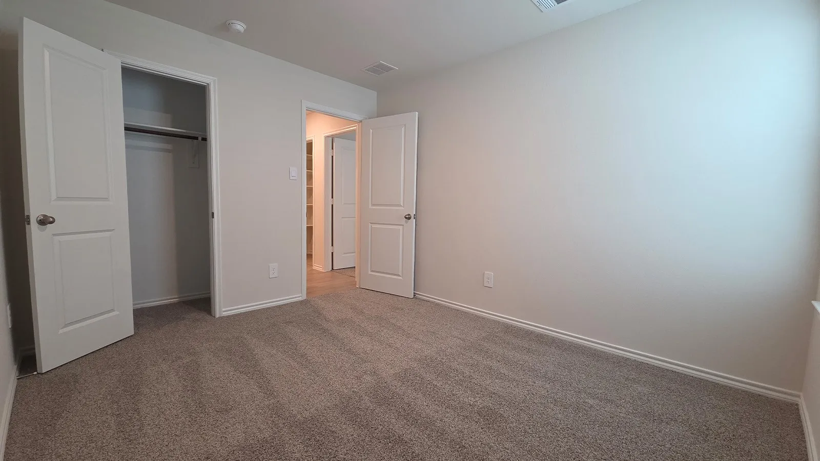 Carpeted interior room featuring neutral wall paint, white trim, and a double-door closet with a hanging rod