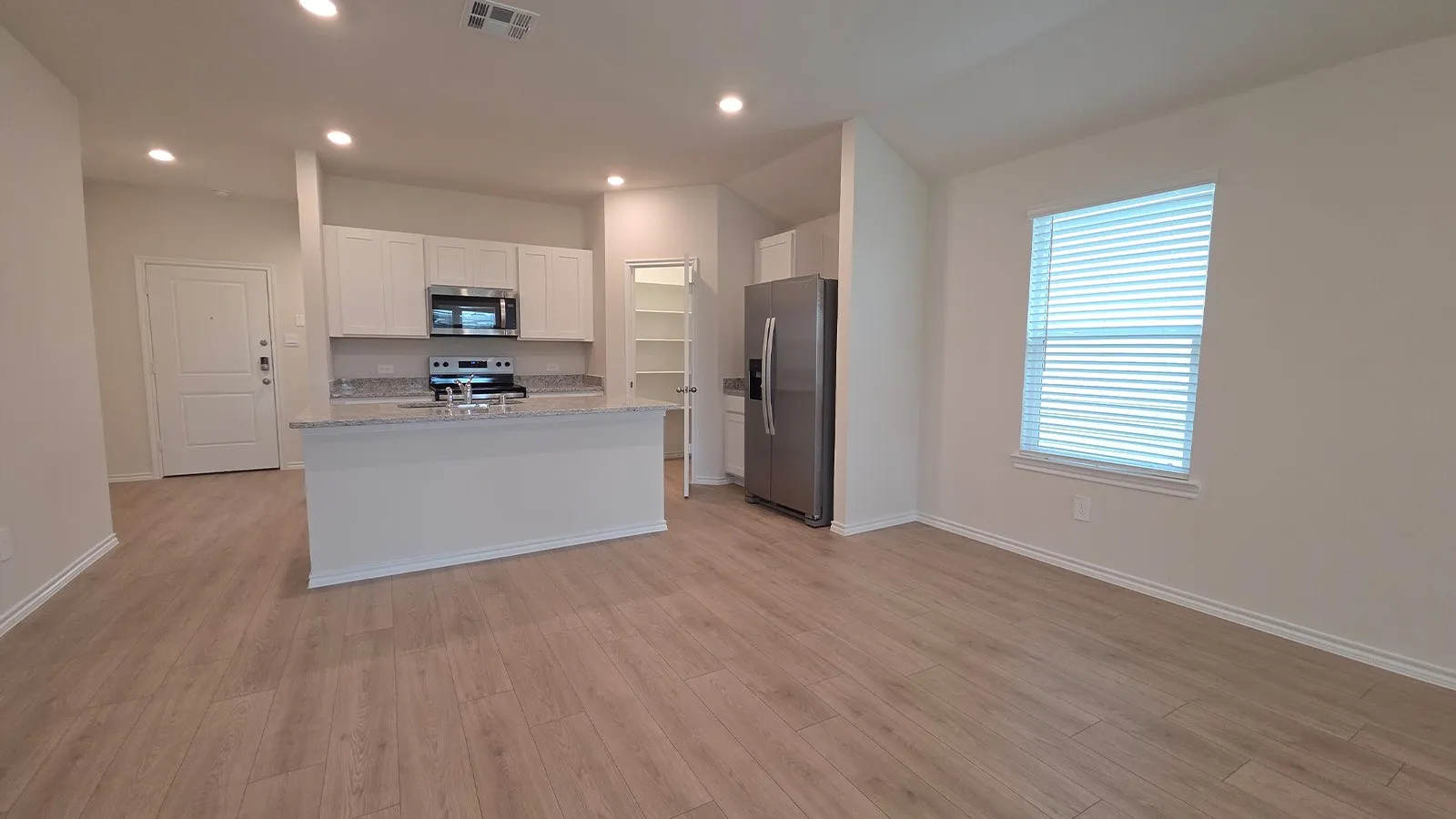 Open-concept living space with wood-finish flooring, recessed lighting, and a kitchen island featuring a breakfast bar