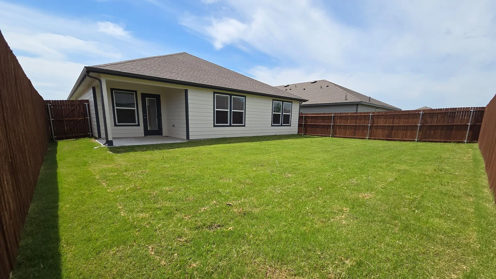 Expansive backyard featuring a manicured lawn, full privacy fencing, and a concrete patio