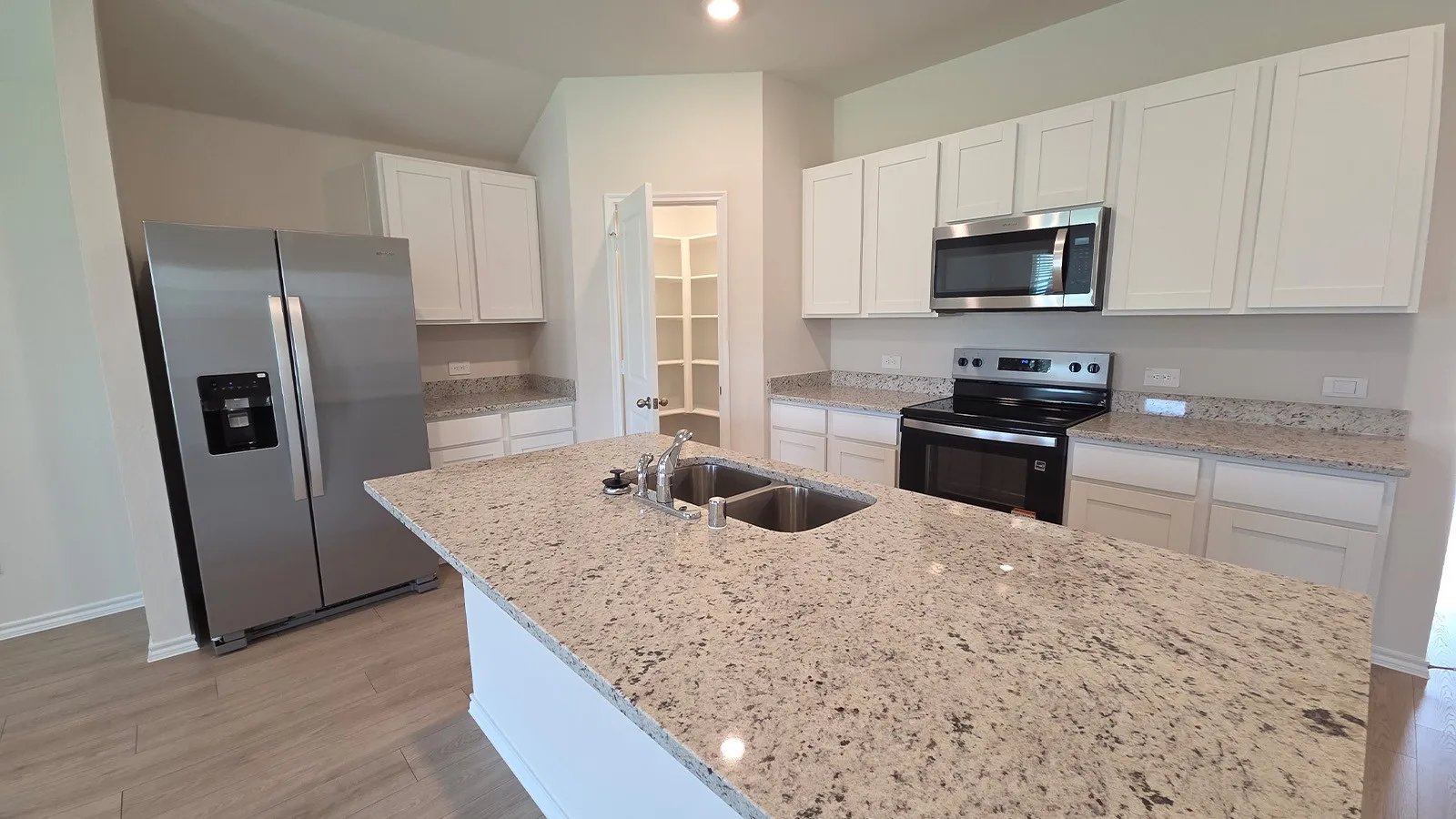 Kitchen featuring a central island with a double basin sink, light-colored granite countertops, white cabinetry, stainless steel appliances, and wood-finish flooring