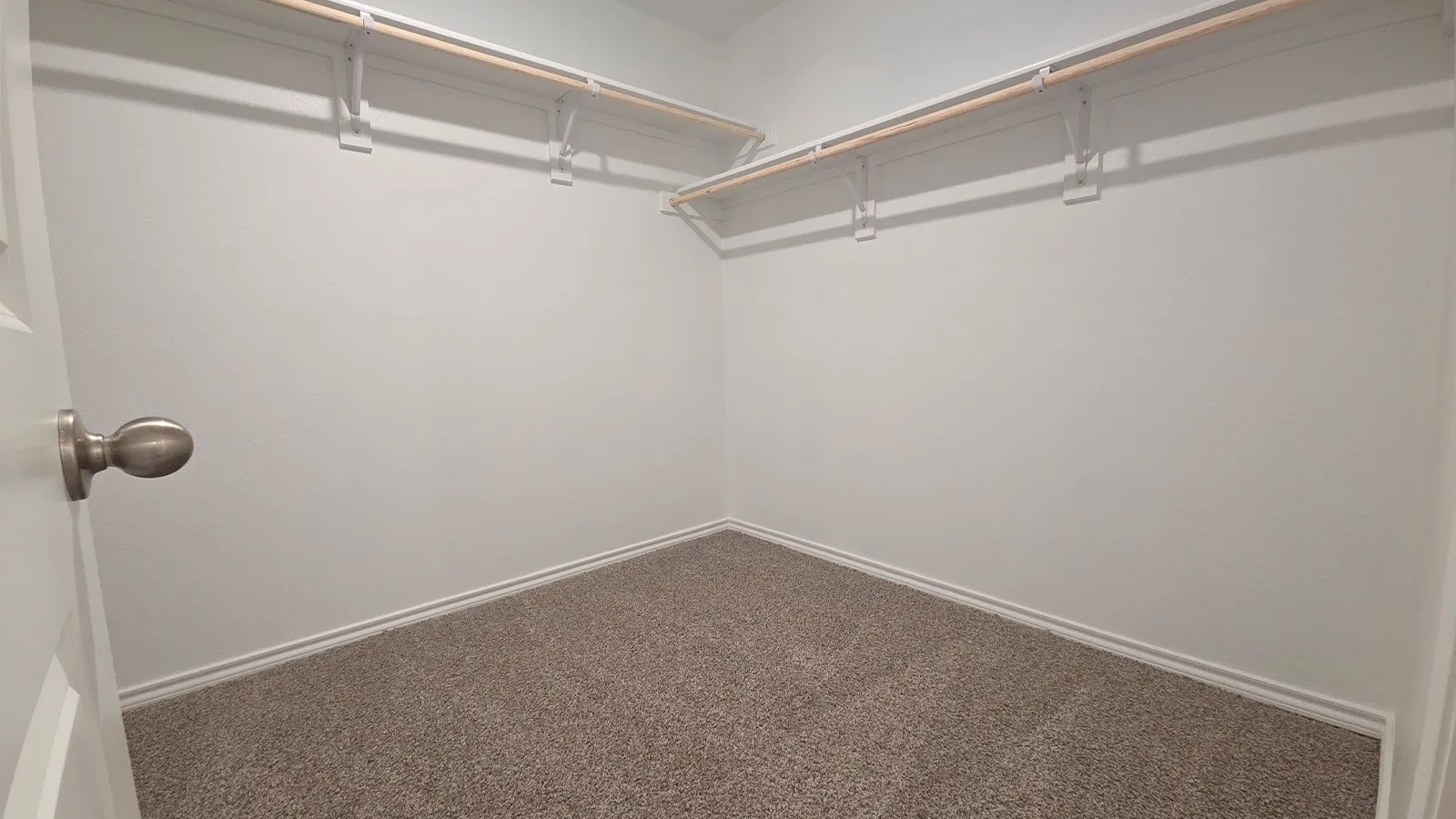 Spacious walk-in closet featuring light gray carpeting, white walls, and built-in white wire shelving with wood rods