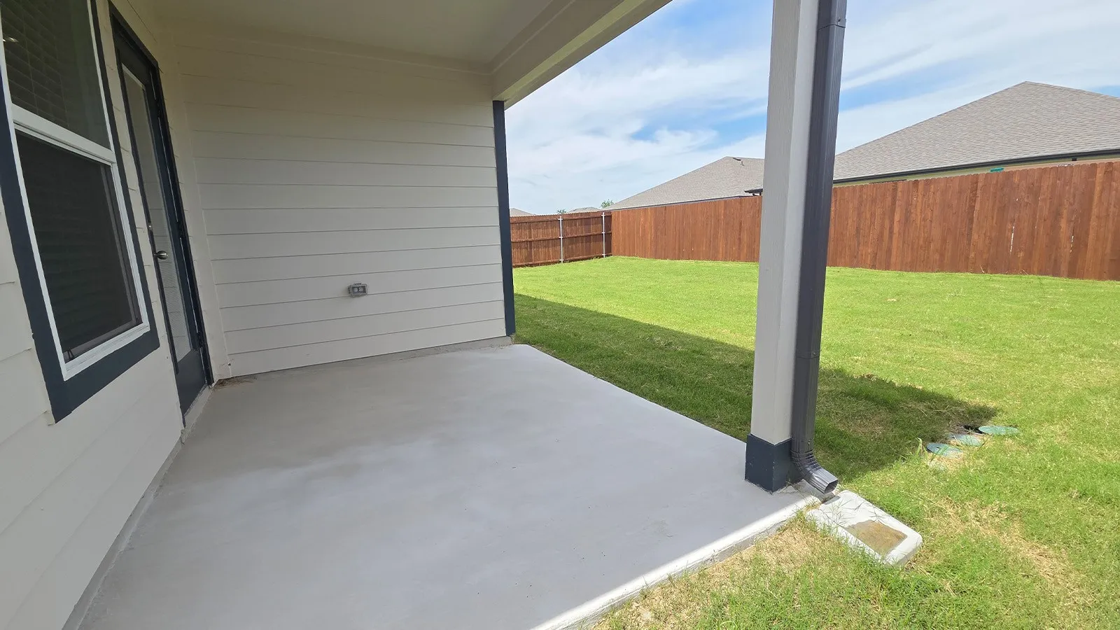 Covered concrete patio opening to a spacious grassy yard