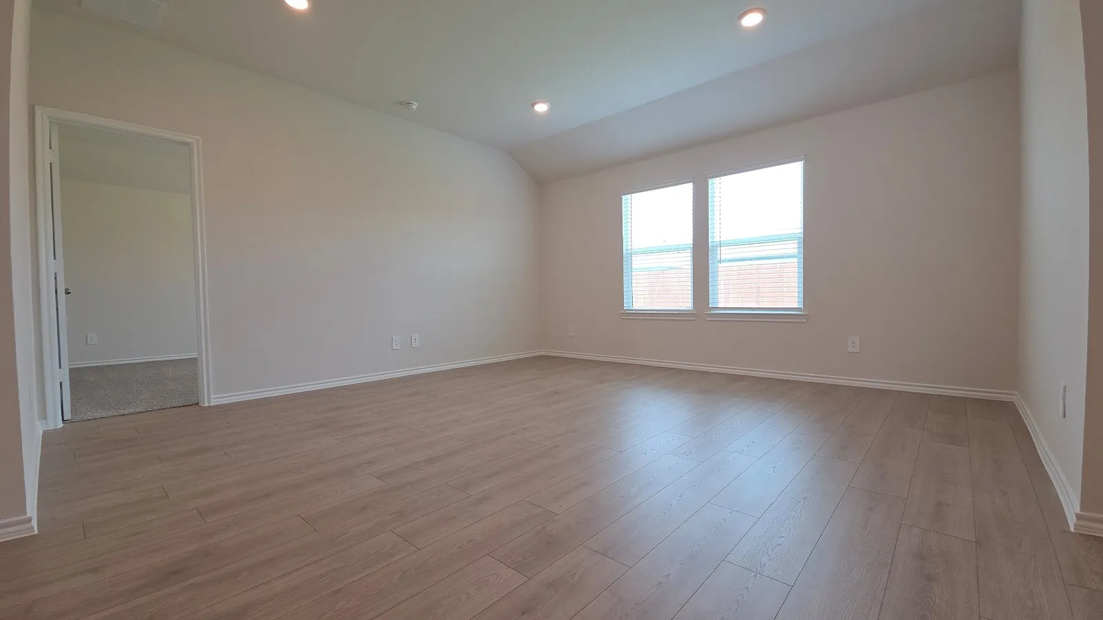 Spacious interior room featuring light wood-finish flooring, recessed lighting, and two windows with white blinds