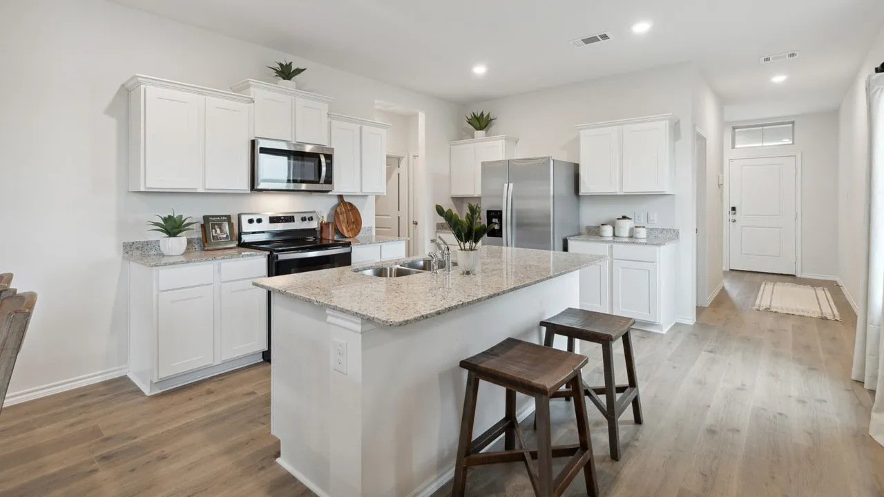 Bright kitchen featuring white cabinetry, stainless steel appliances, a multi-tone countertop, an island with a dual-basin sink, and wood-finish flooring
