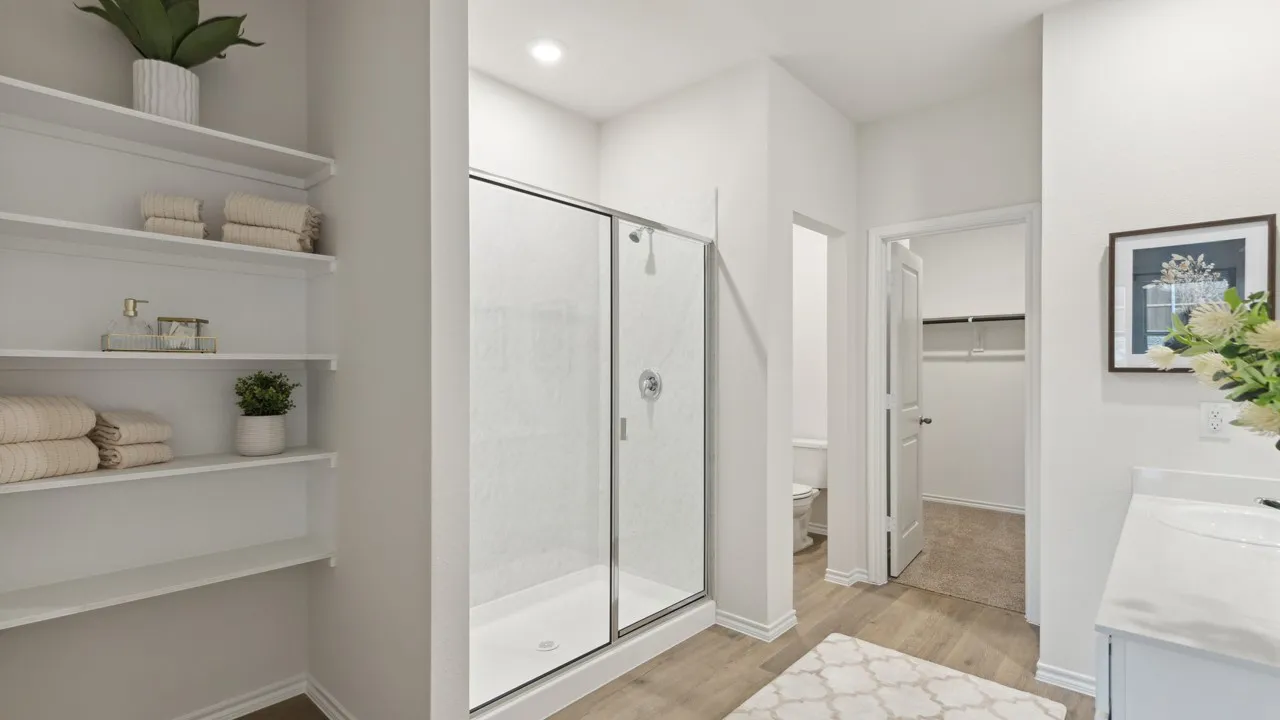 Spacious bath featuring wood-finish flooring, a glass-enclosed shower with tile surround, built-in shelving, and a vanity with a countertop
