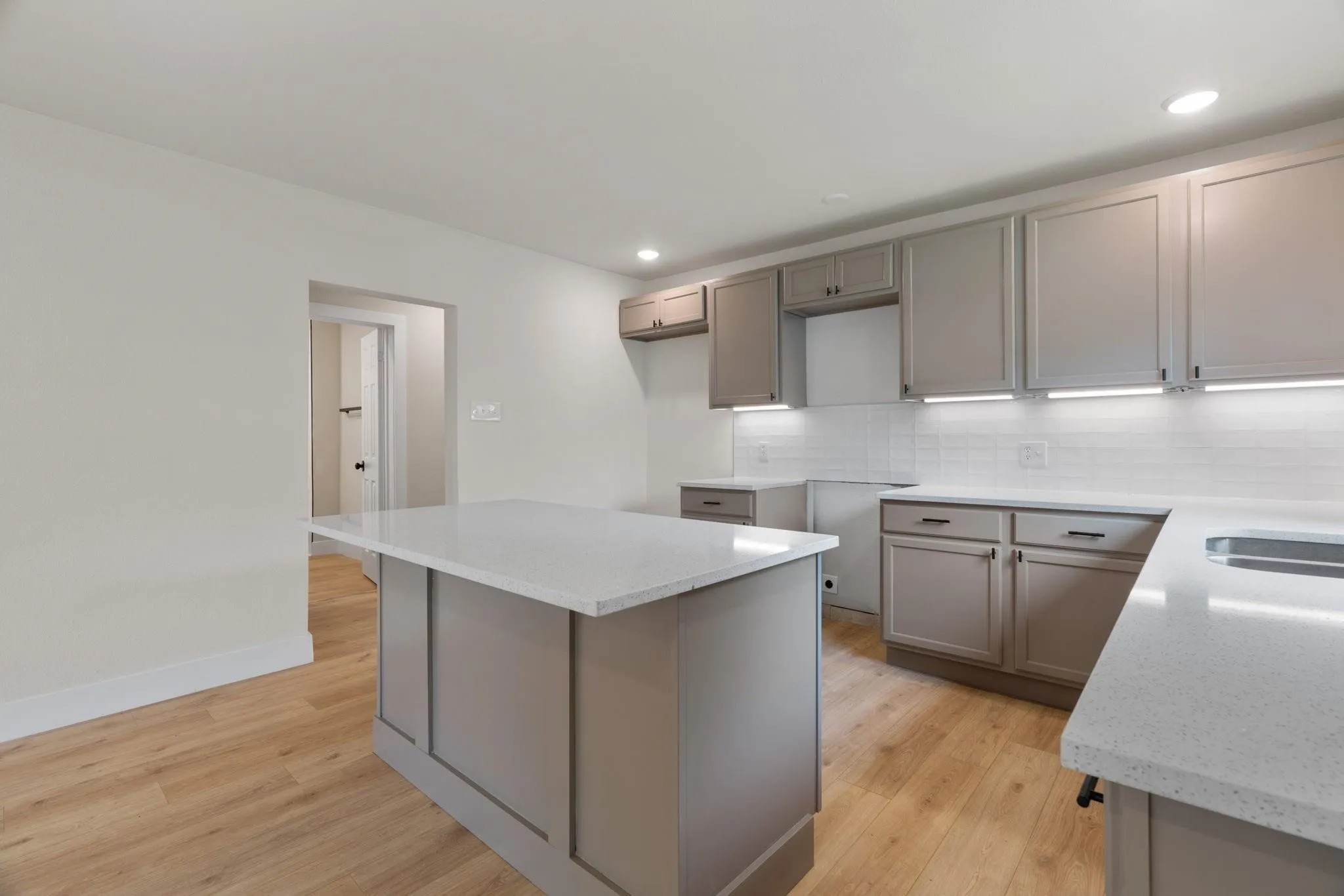 Modern kitchen featuring a central island with a light-toned countertop, gray shaker-style cabinetry, and a white subway tile backsplash