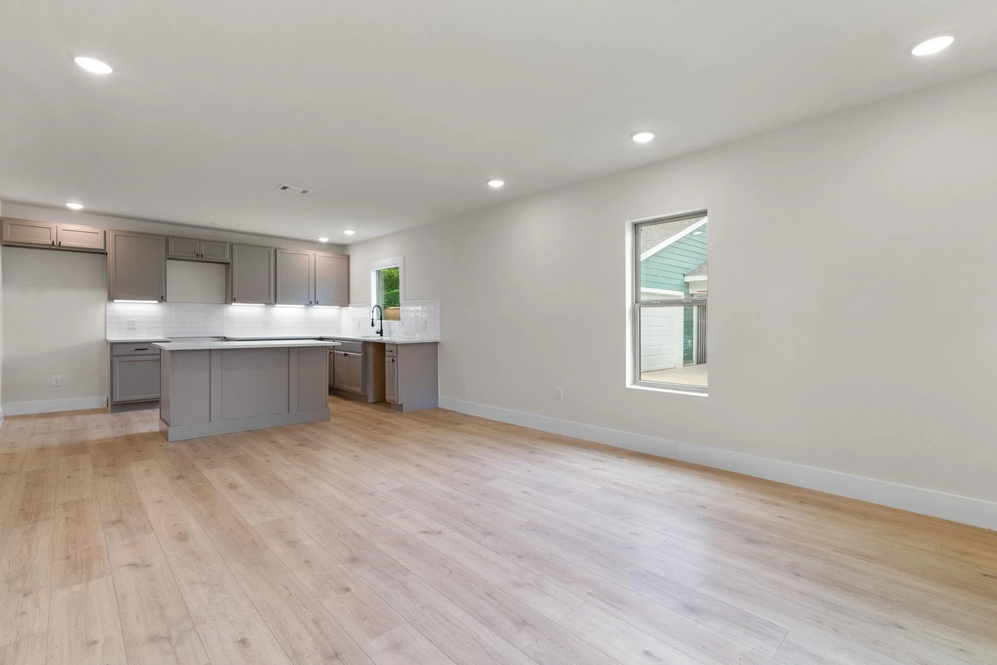 Kitchen featuring gray cabinetry, a center island, a sink, tasteful backsplash, and light wood-type flooring