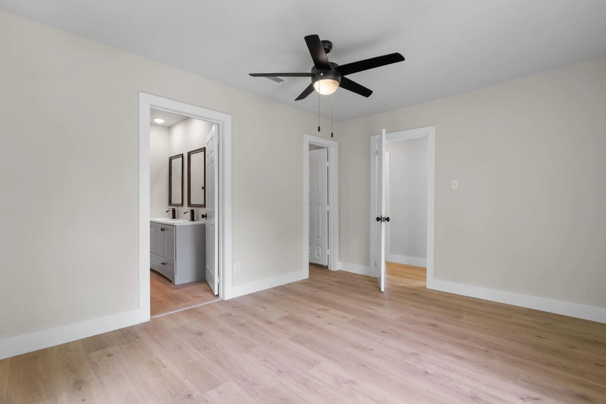 Unfurnished bedroom with light wood-style flooring, baseboards, ensuite bath, and ceiling fan