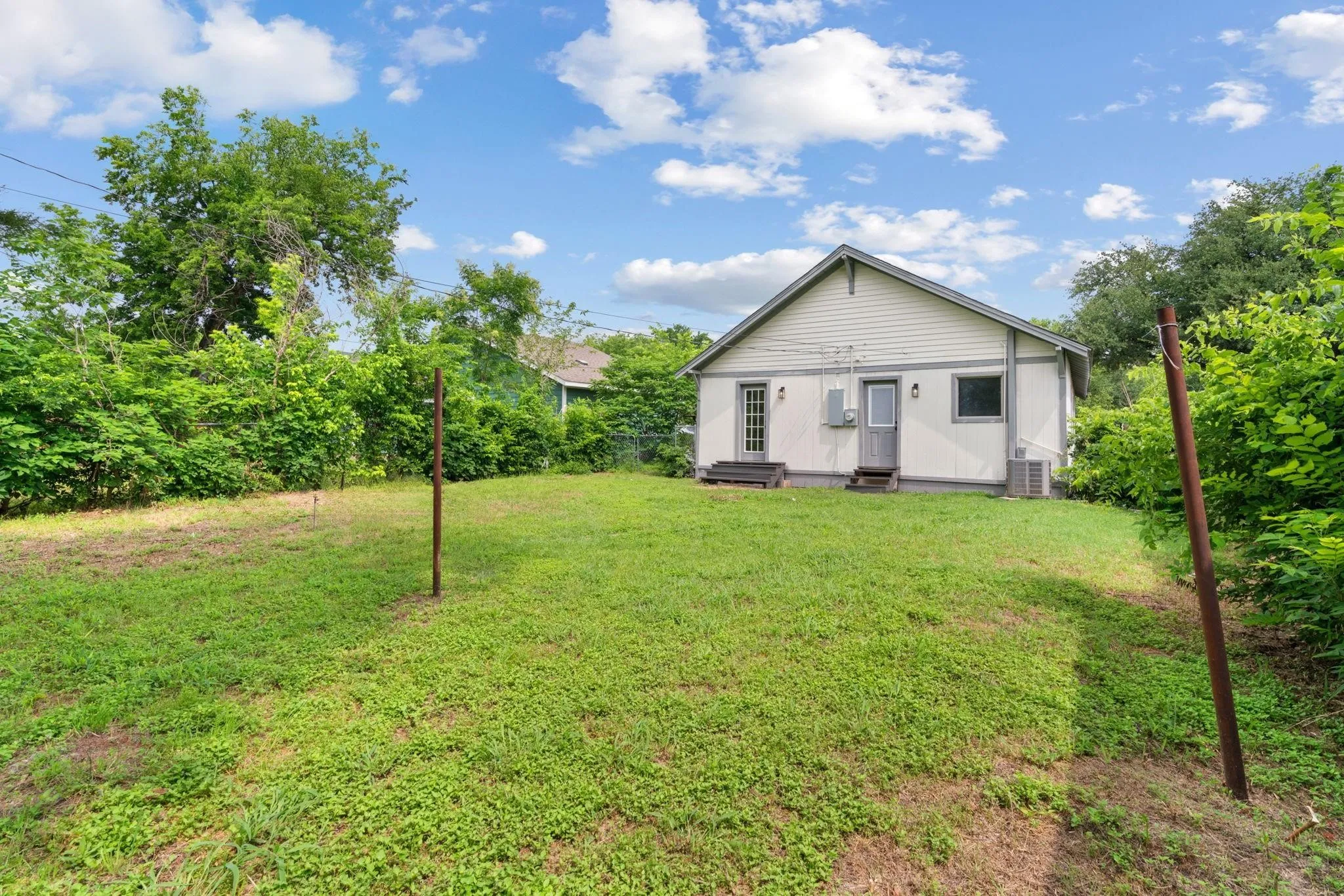 Spacious rear yard with a neutral-toned exterior, two entry doors, and mature perimeter landscaping