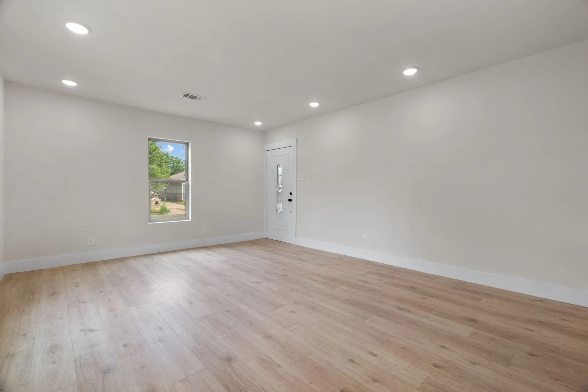 Spacious room featuring light wood-finish flooring, recessed lighting, and a white entry door with frosted glass inserts