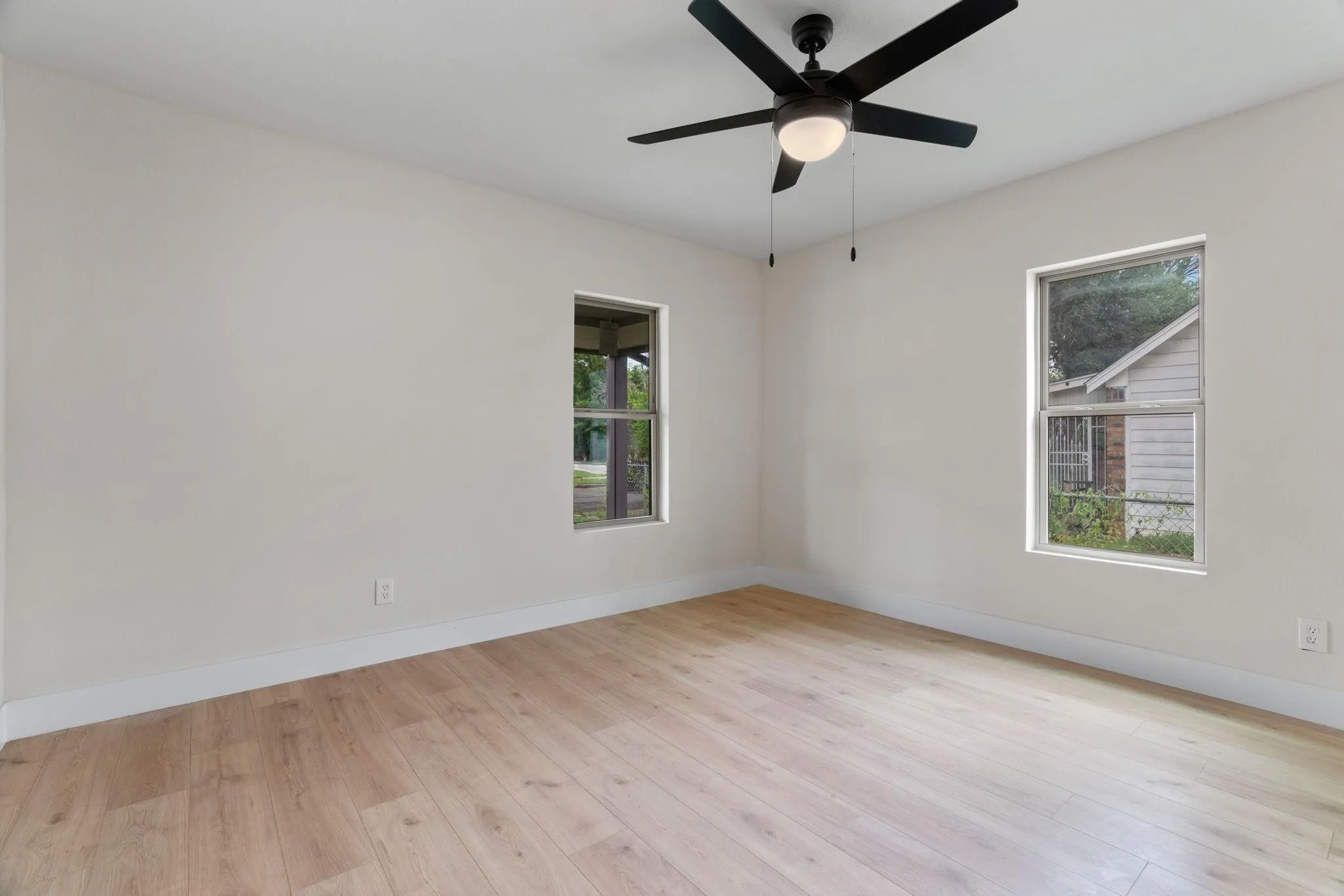 Light-filled room featuring wood-finish flooring, a modern black ceiling fan with integrated lighting, and two windows
